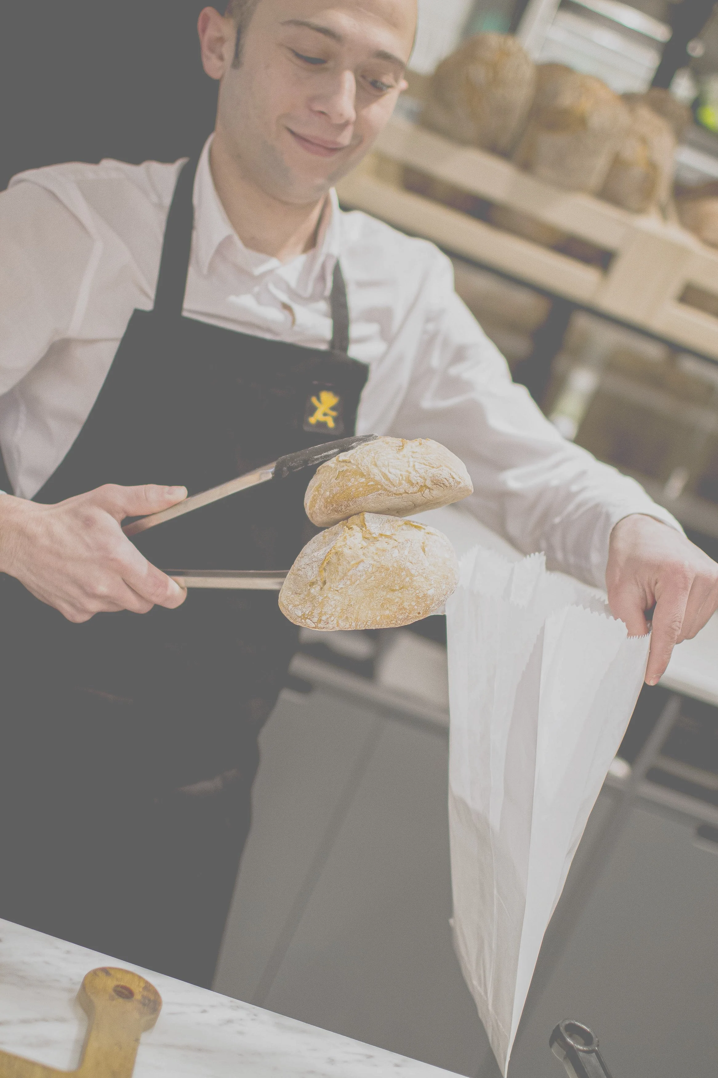 Mann beim Einpacken von frischem Brot in eine Papiertragetasche in einer Bäckerei.