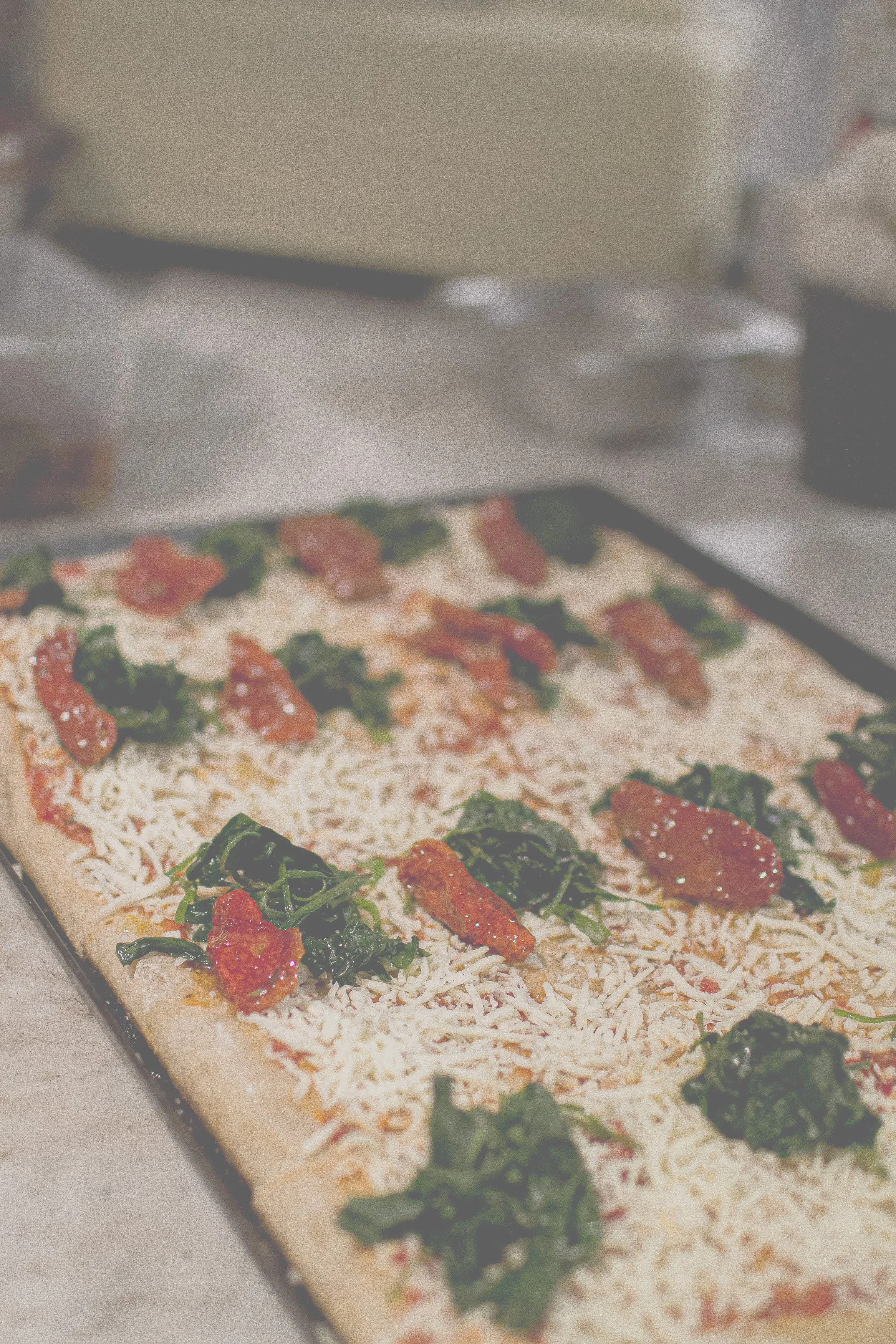 Un ungebackener flacher Teig mit Tomatenscheiben, geriebenem Käse und frischem Basilikum auf einem Backblech.