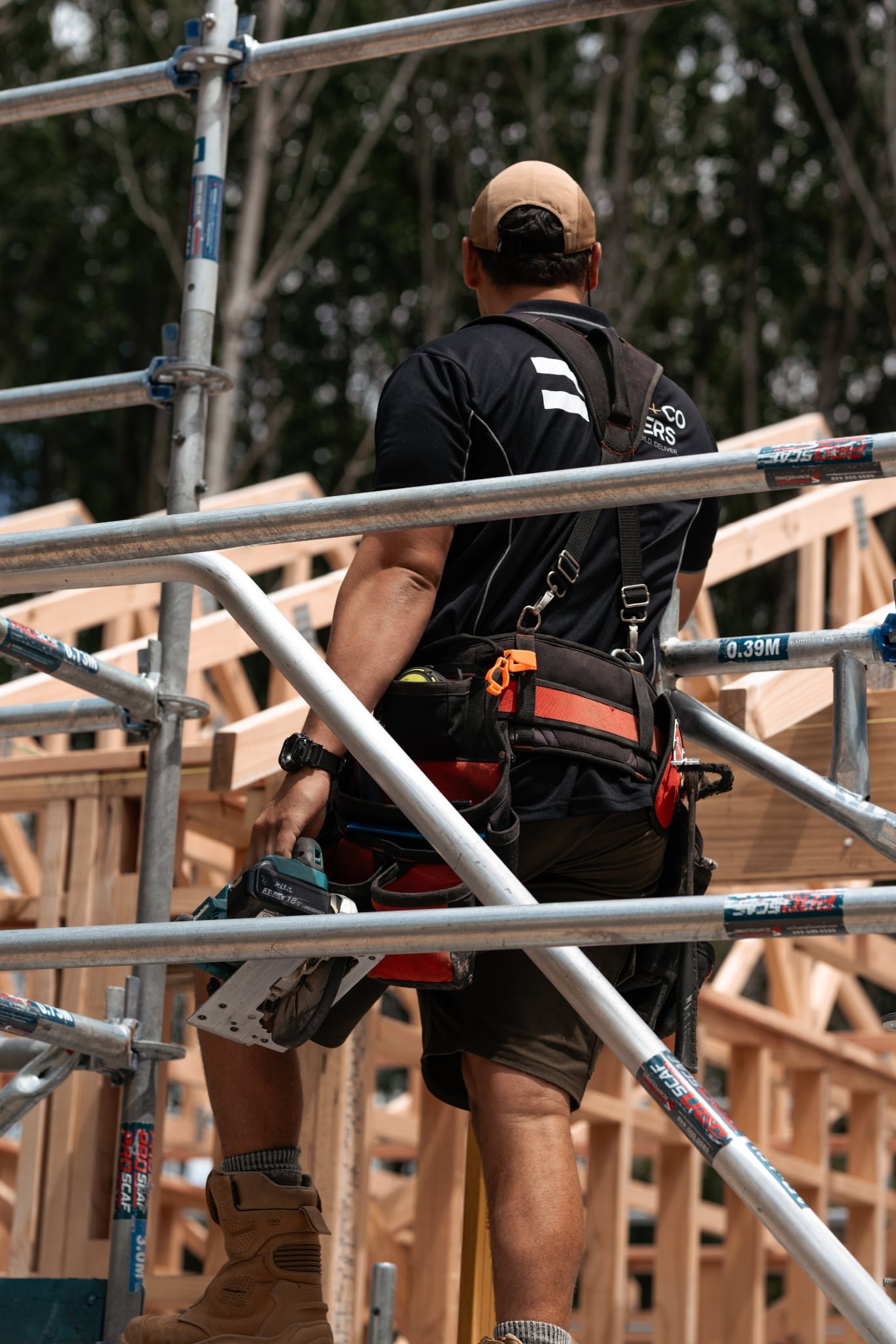 A construction worker stands on scaffolding at a building site with wooden framing in the background.