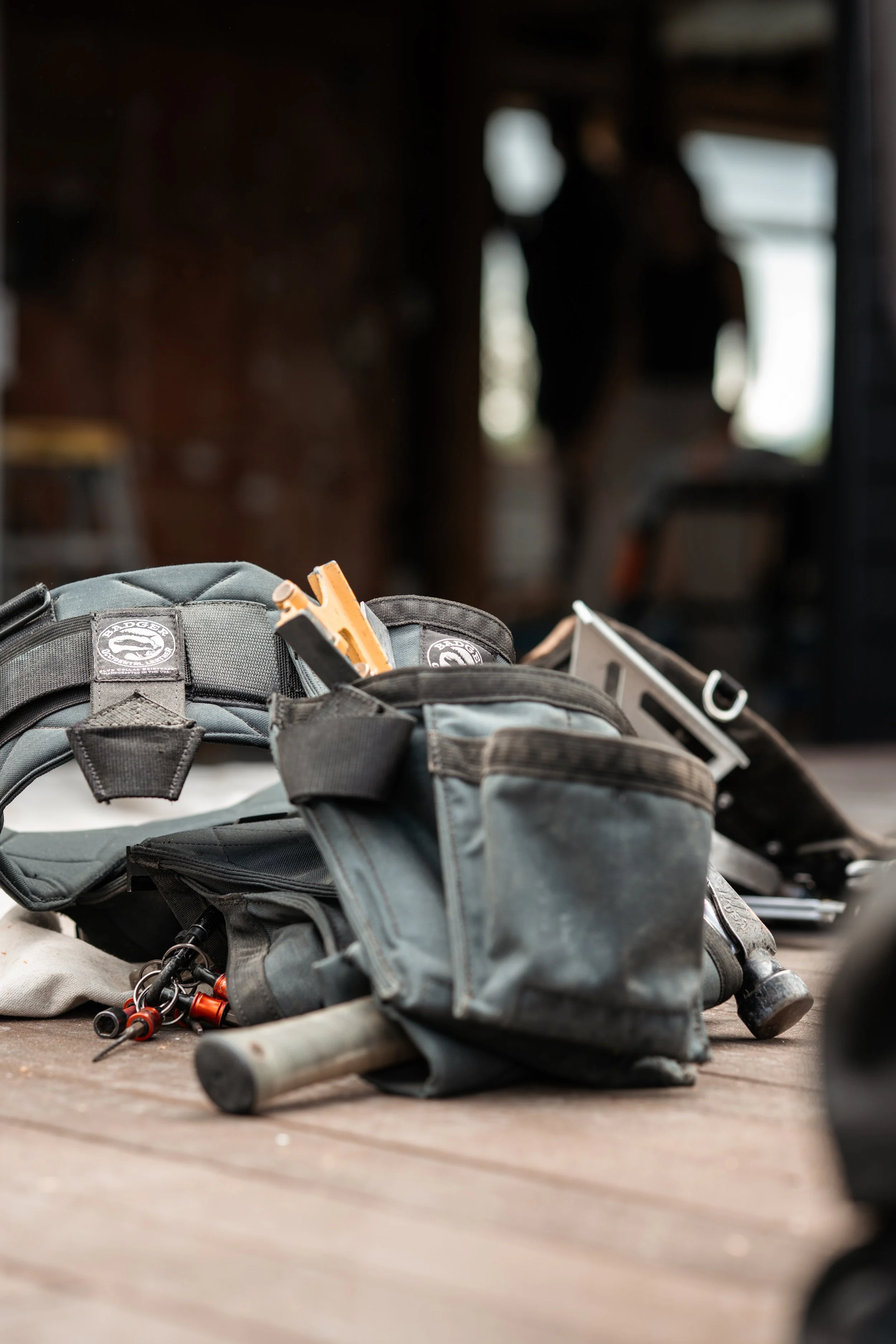 Tools and equipment scattered on a wooden surface, including a hammer, screwdrivers, and a pocket knife, with blurred figures of people in the background.