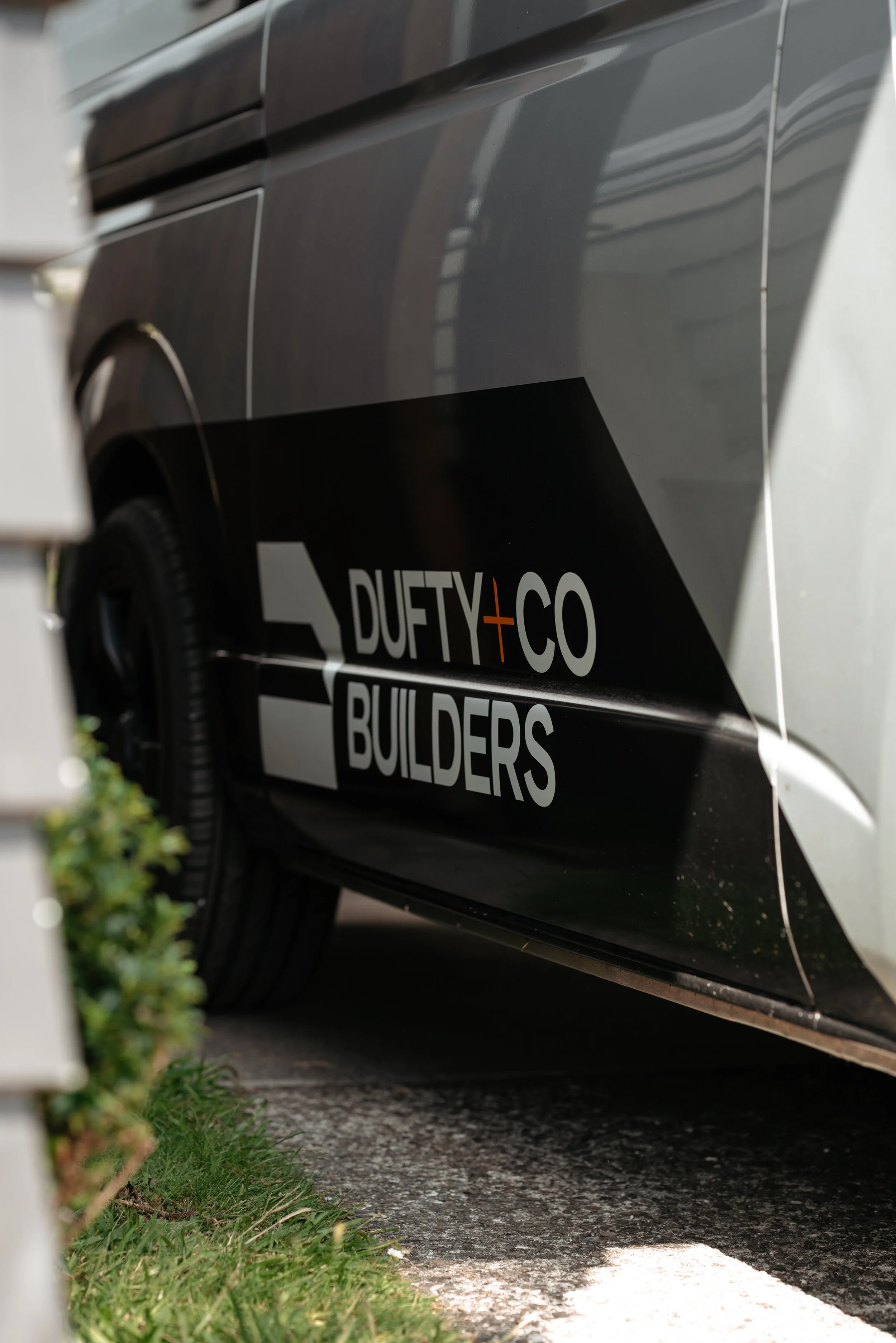 Close-up of a vehicle with a black and white graphic decal that reads 'DUFTY + CO BUILDERS'.