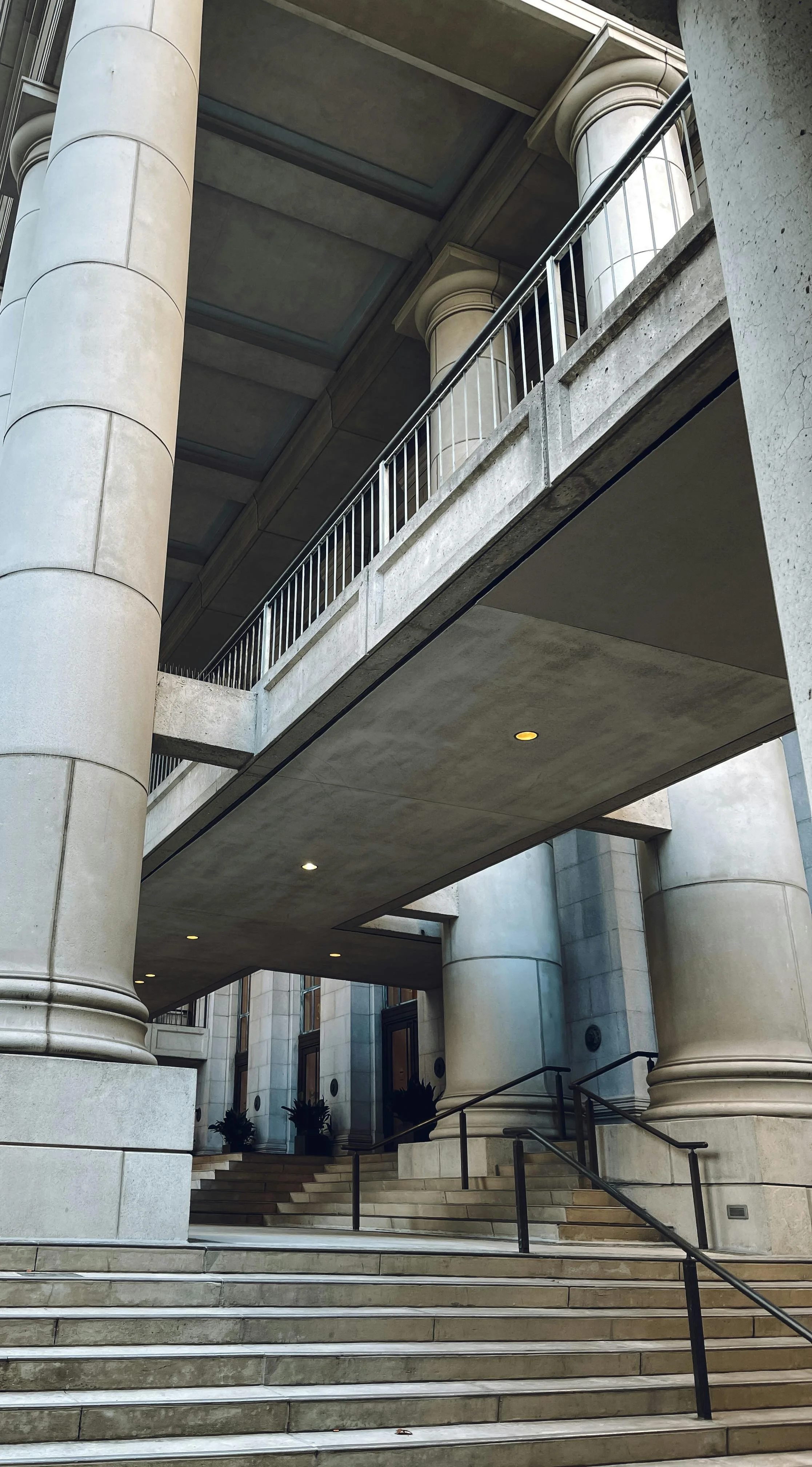 Exterior of a large building with stone columns, stairs, and a covered walkway, featuring classical architectural design.