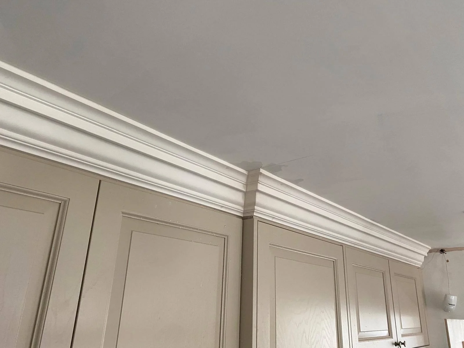 A corner of a room with beige cabinets and white crown molding, and a small section of a gray ceiling with a water stain.