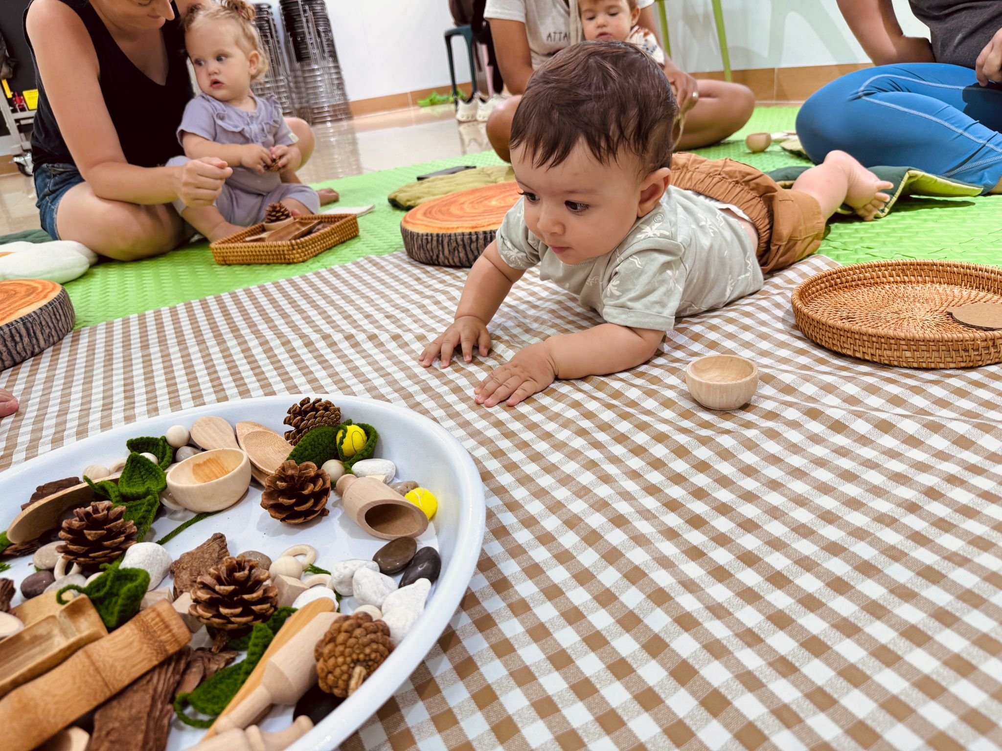 Children playing with natural and wooden toys on a checkered mat in a playroom.