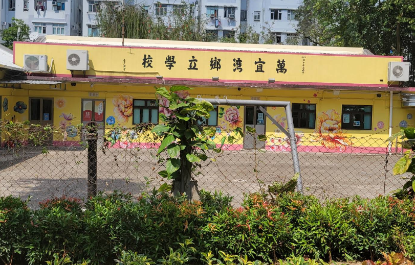 School building with yellow walls and floral mural, fenced courtyard, and a sign with Chinese characters.