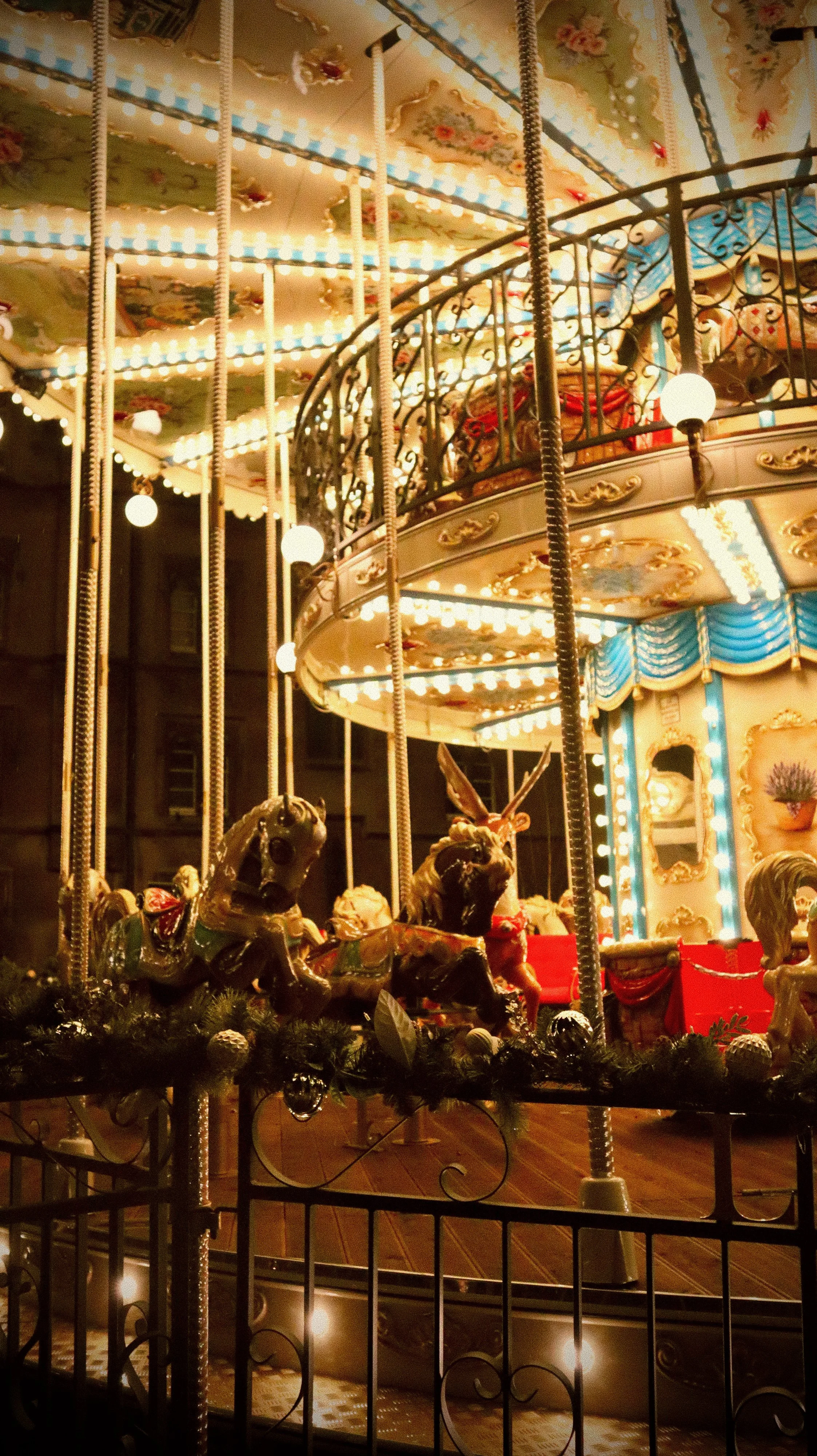 A brightly lit vintage carousel with painted carousel animals, including a horse and a rabbit, decorated with festive ornaments at night.