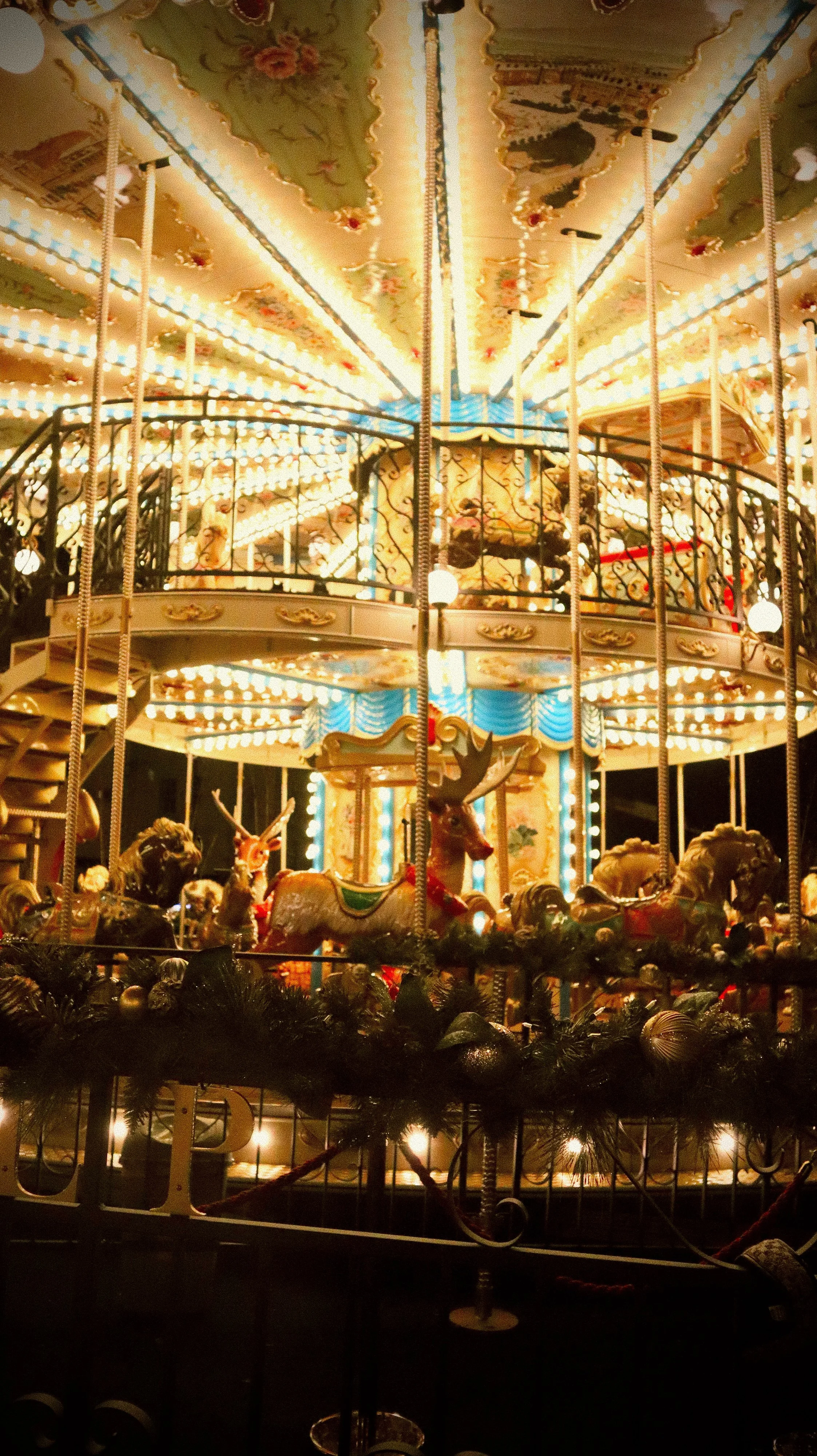 A brightly lit vintage carousel with painted animals, including a reindeer, horses, and a deer, decorated with lights and holiday decorations, at night.