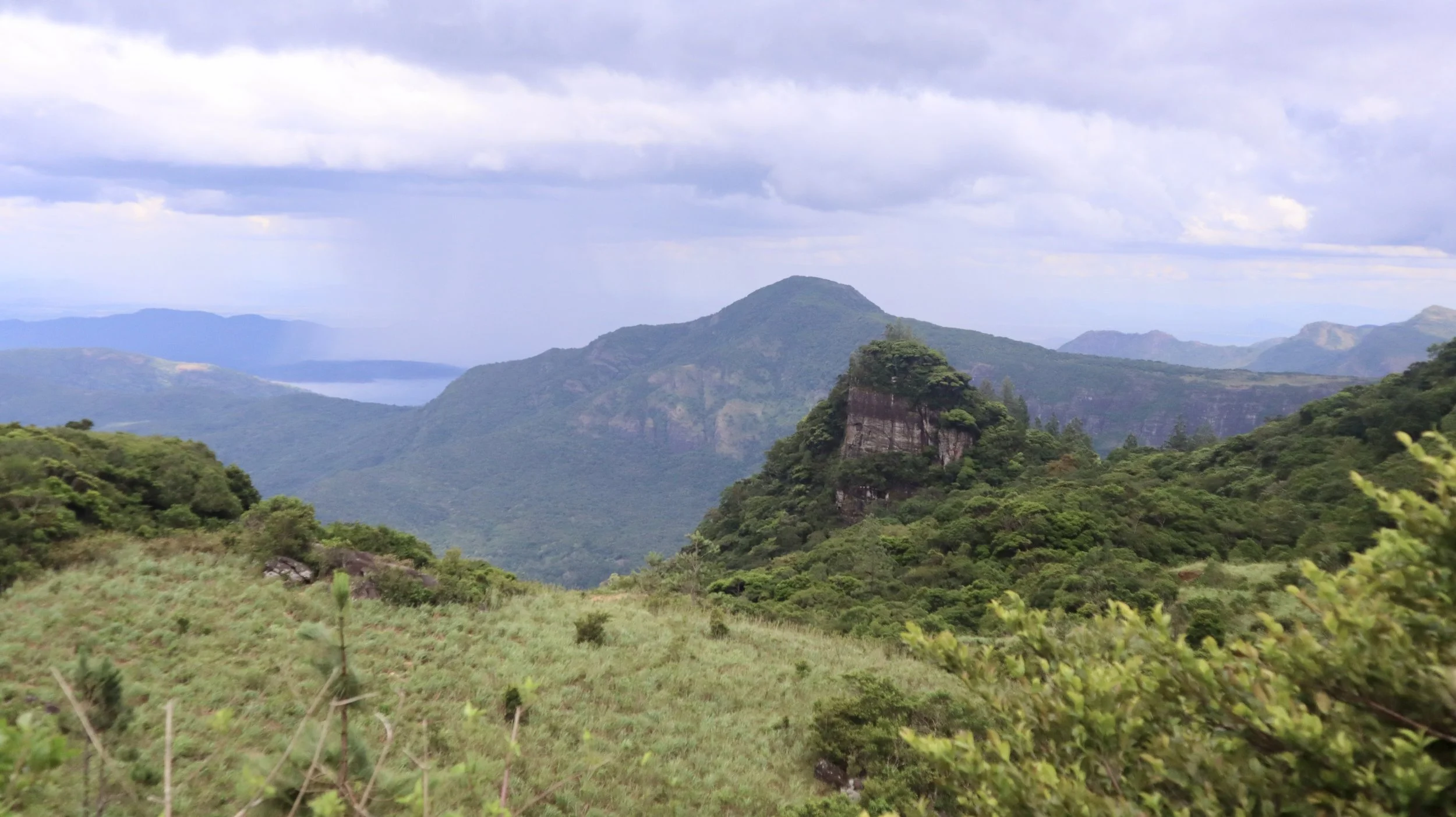 Lush green mountains with a rock formation in the foreground and a cloudy sky overhead.