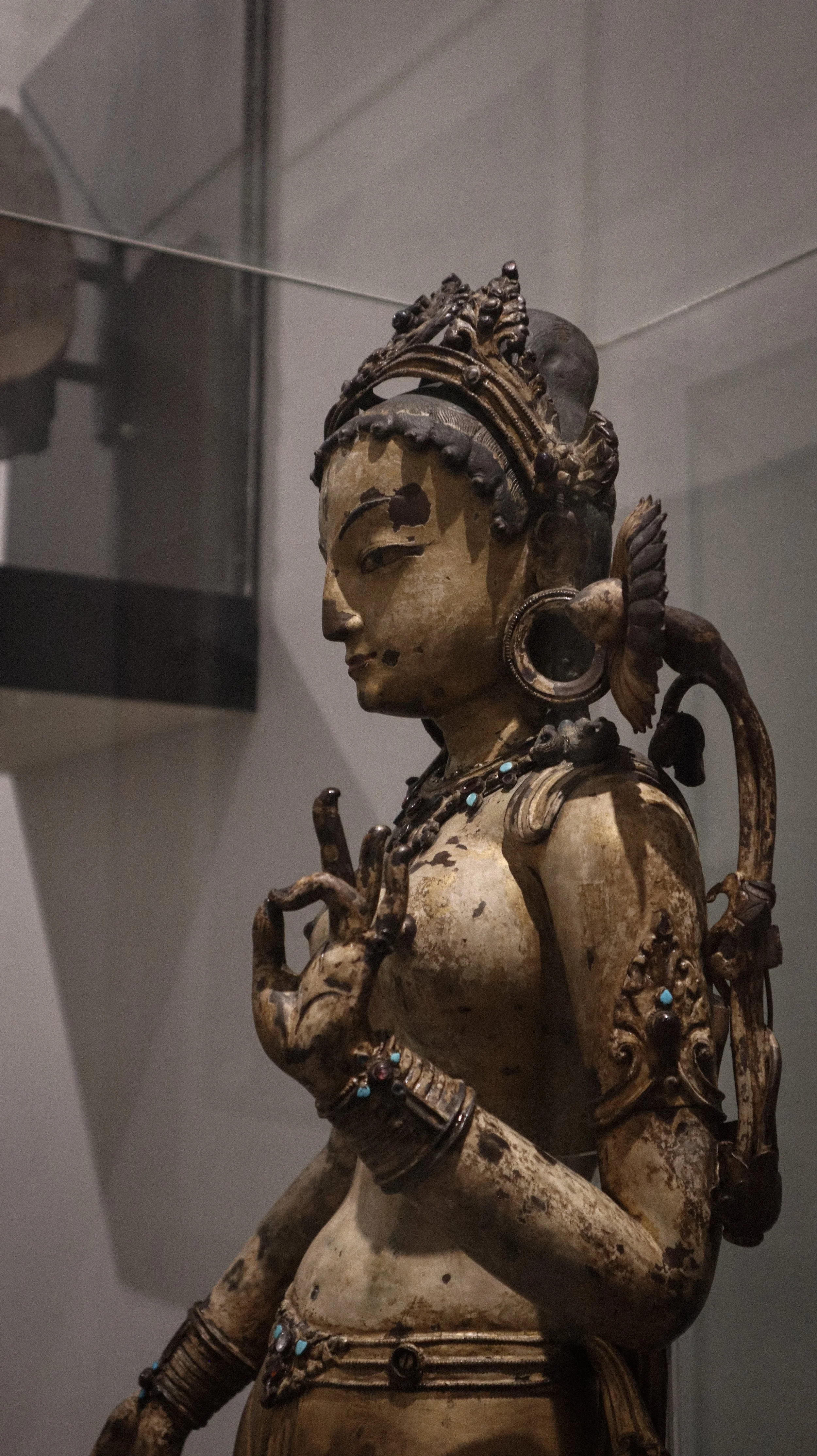A detailed sculpture of a regal woman adorned with jewelry and a crown, with a serene expression, displayed in a museum setting.