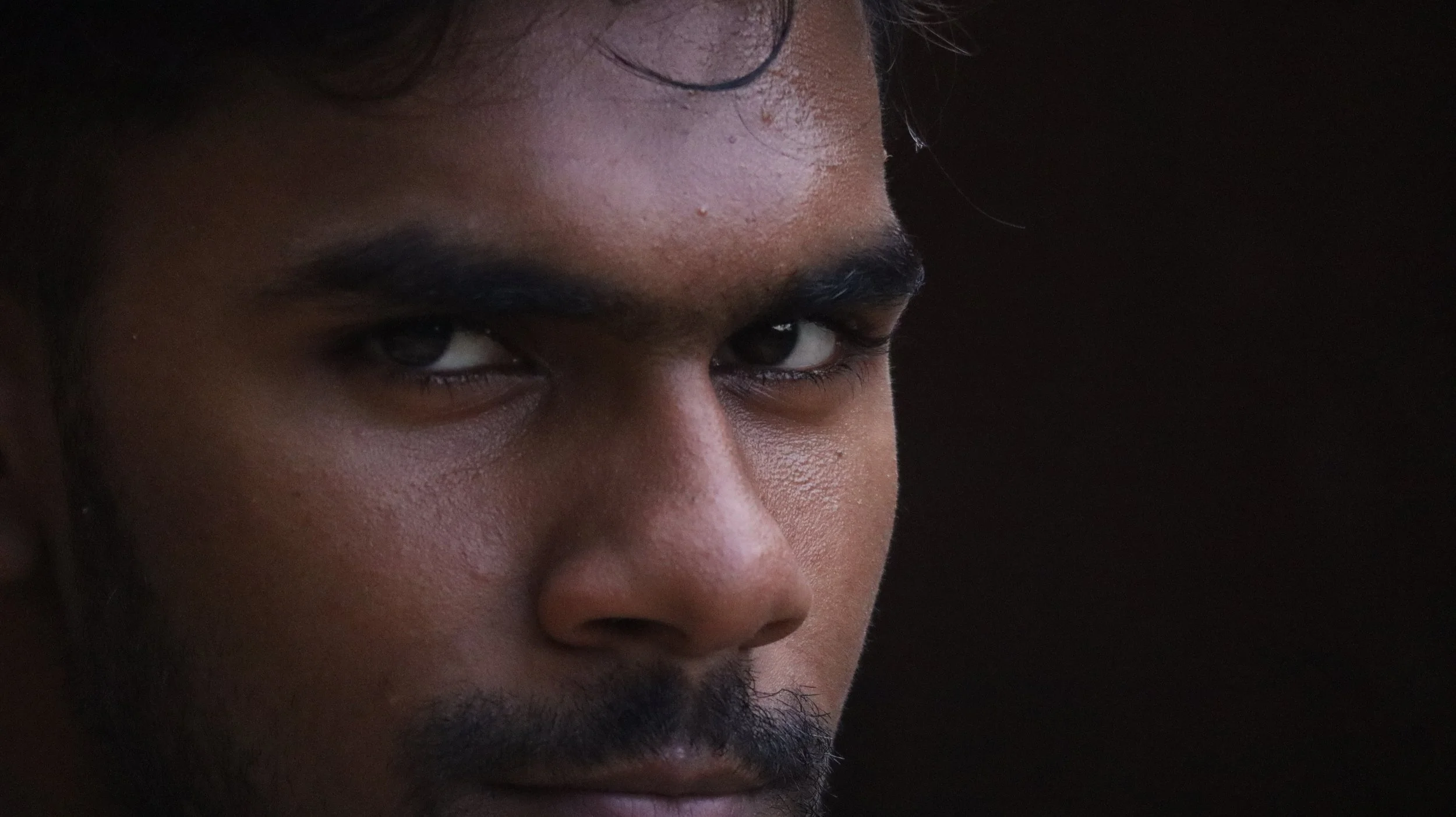 Close-up of a man's face with intense expression, looking directly at the camera, against a dark background.