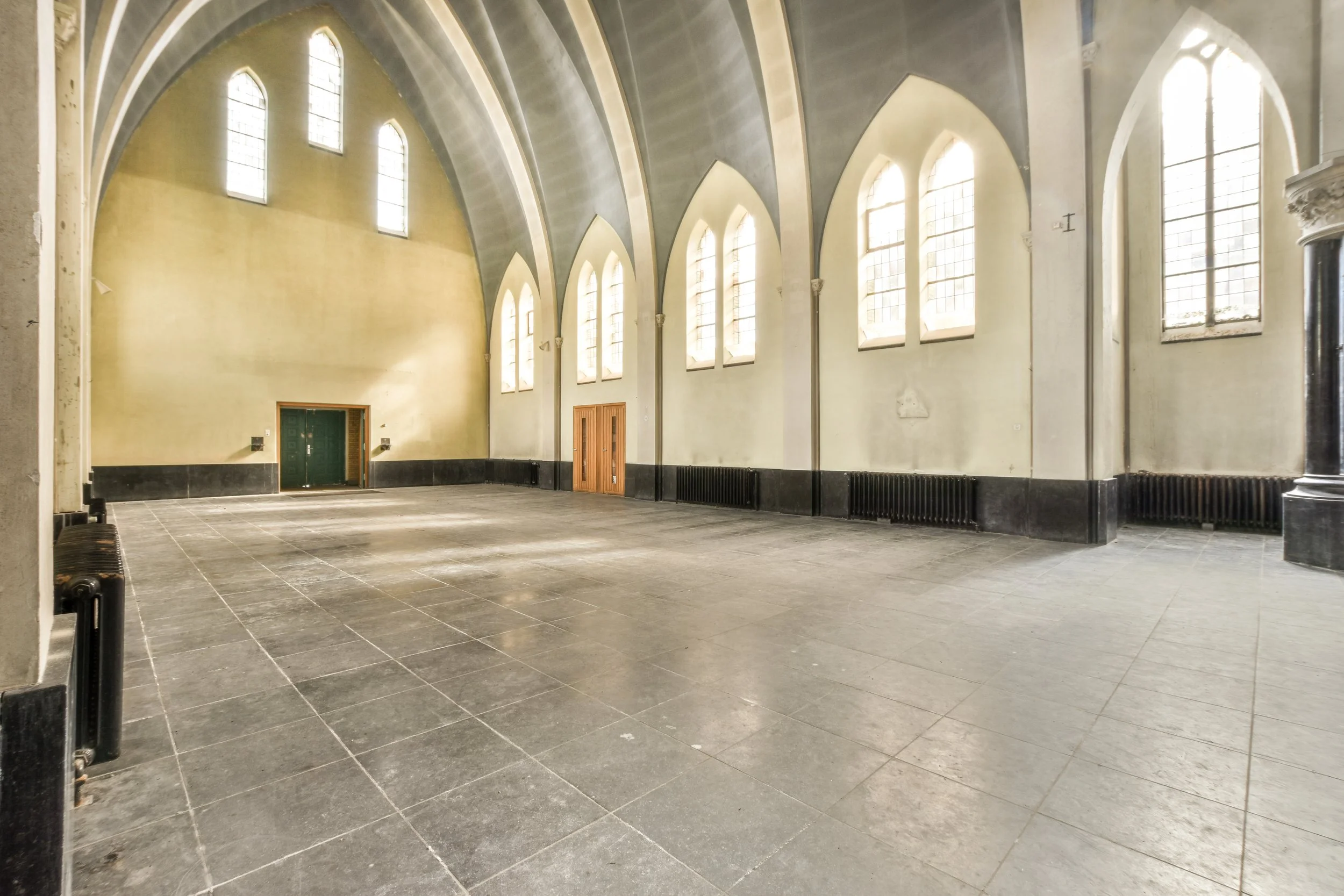 Matterport scan photo of Empty room inside a historic church or cathedral with arched windows and high vaulted ceiling.