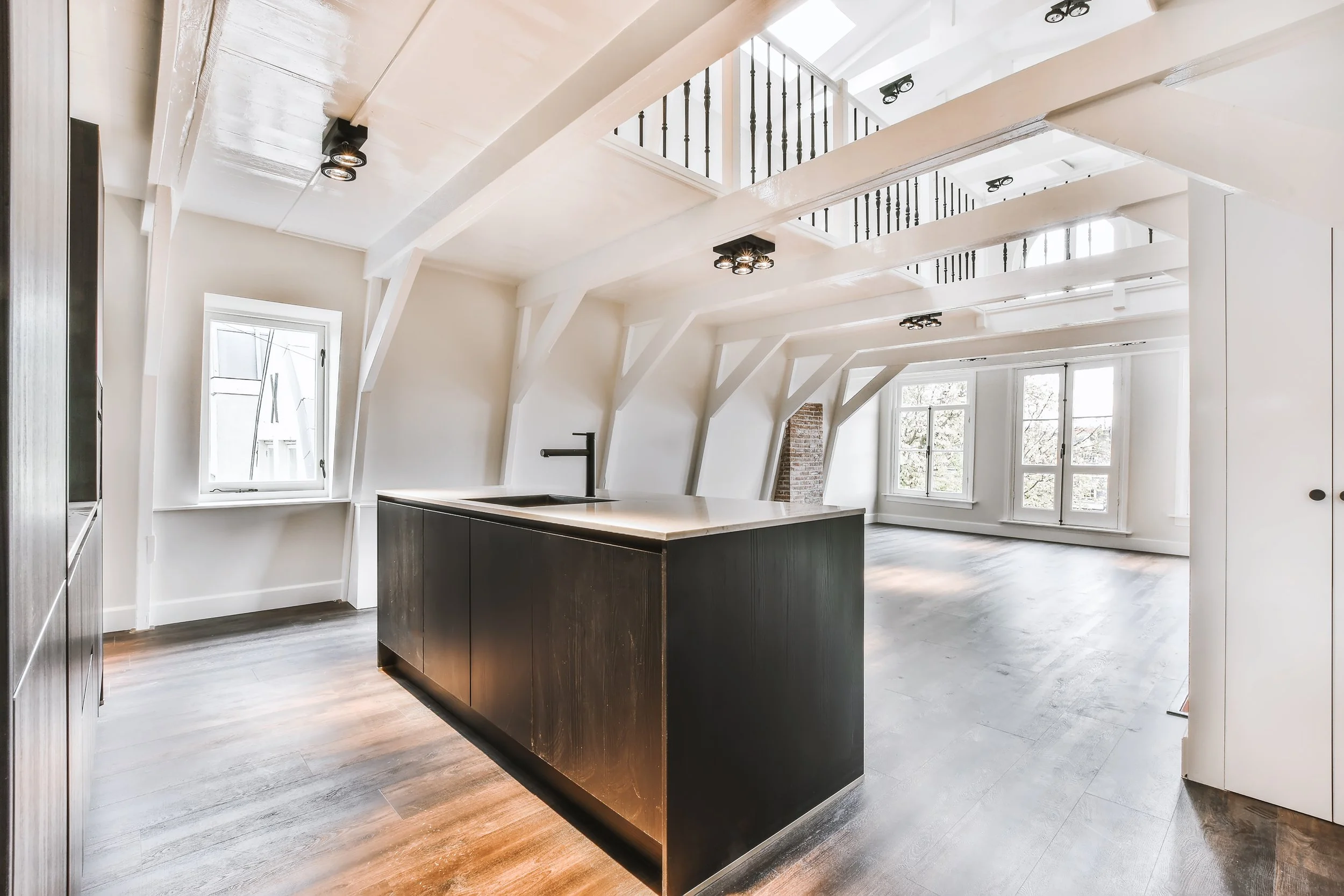 Matterport scan photo of residential home. Bright, open-concept living room with large windows, white walls, exposed beams on the ceiling, and dark hardwood floors.