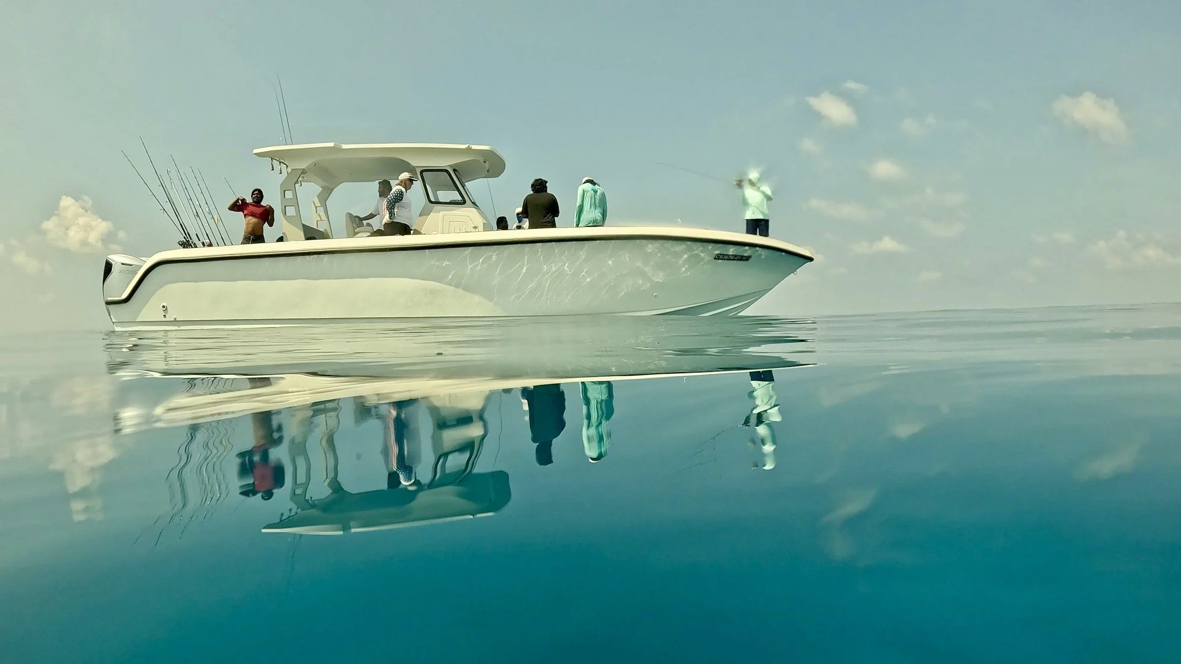 A white recreational boat with several people on board, some standing and one sitting, out on a calm body of water under a partly cloudy sky.