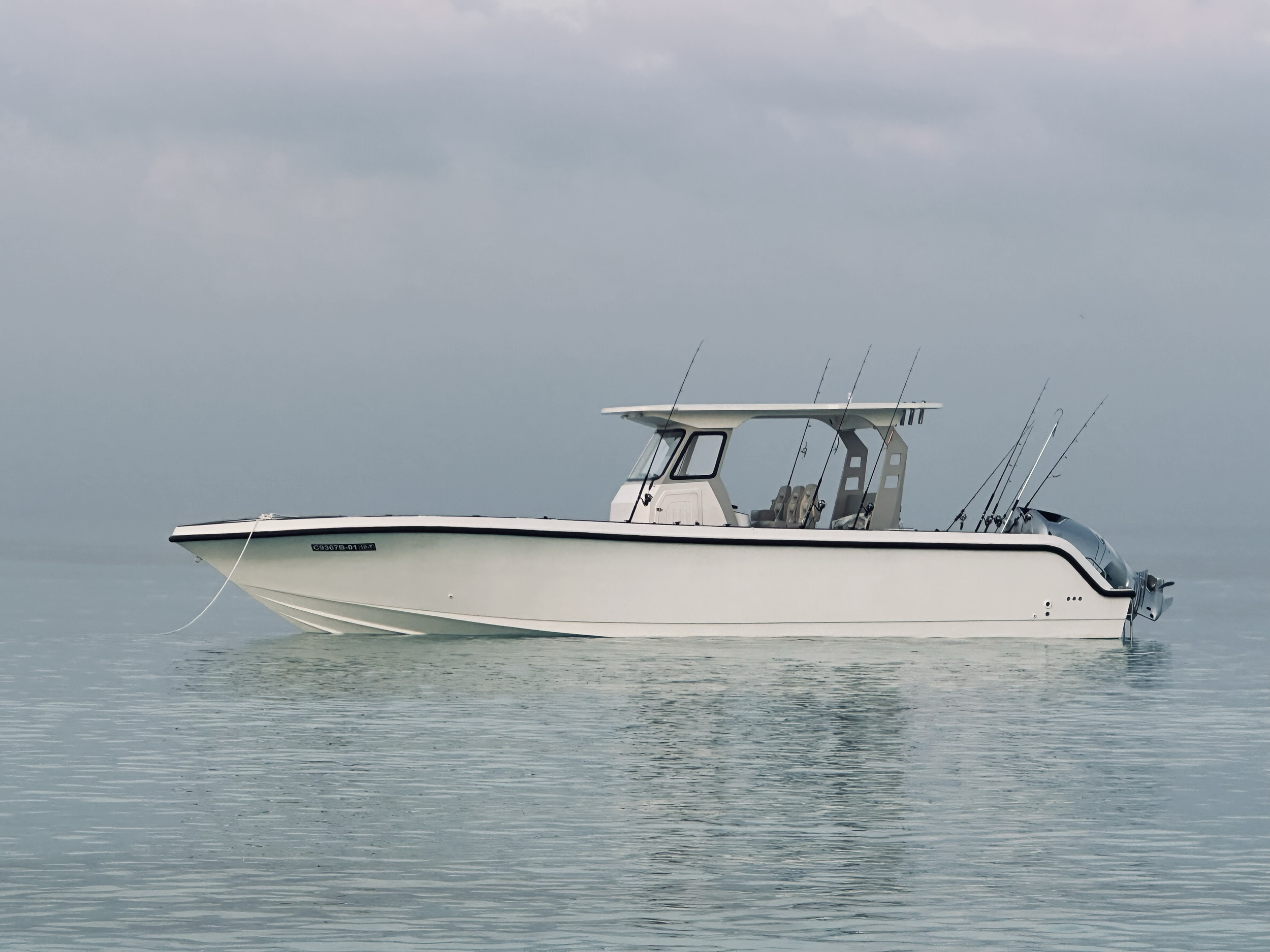 A white fishing boat on calm water with a cloudy sky background.