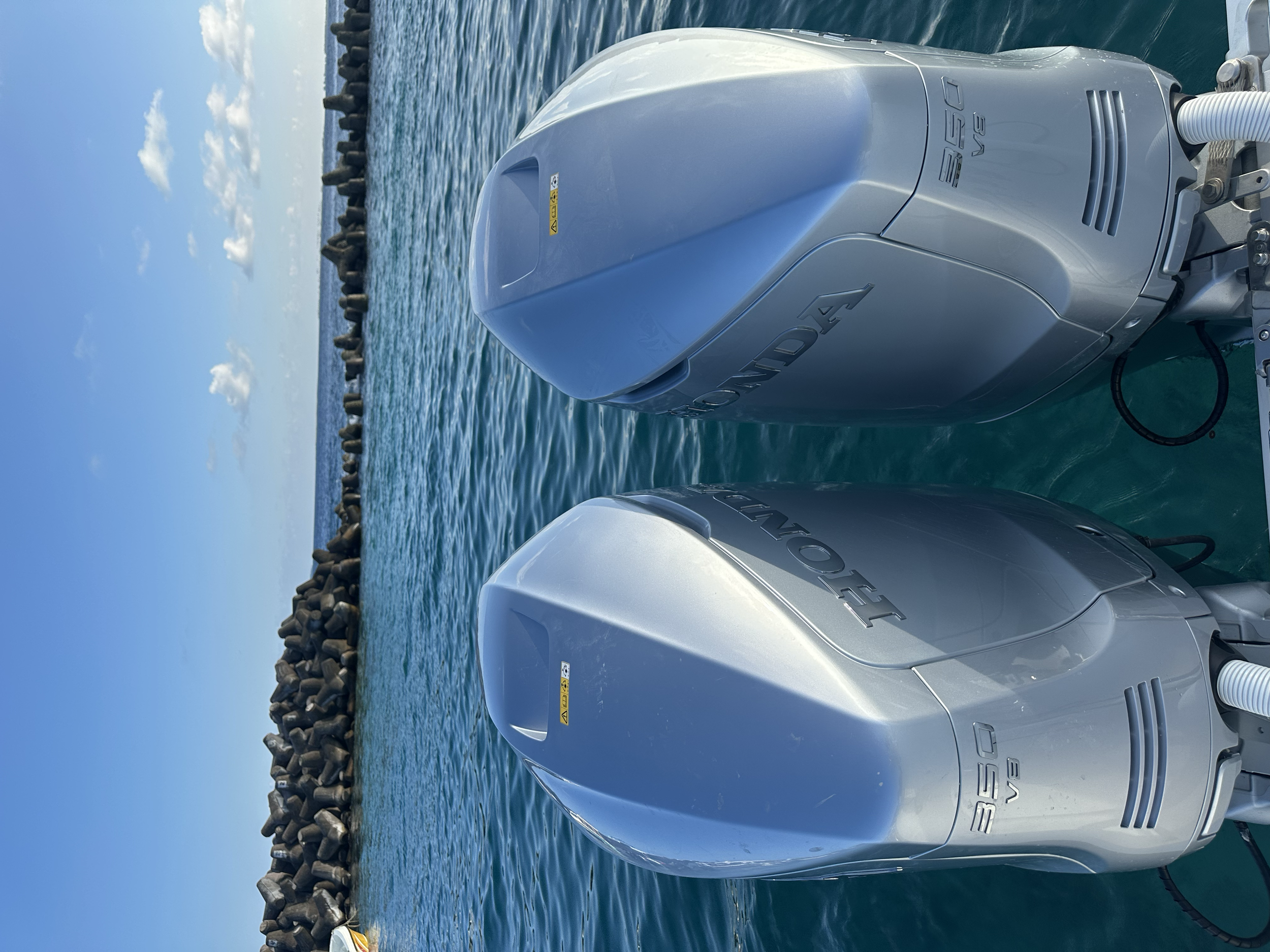 Two Honda outboard motors mounted on a boat in the water, with a breakwater and blue sky in the background.