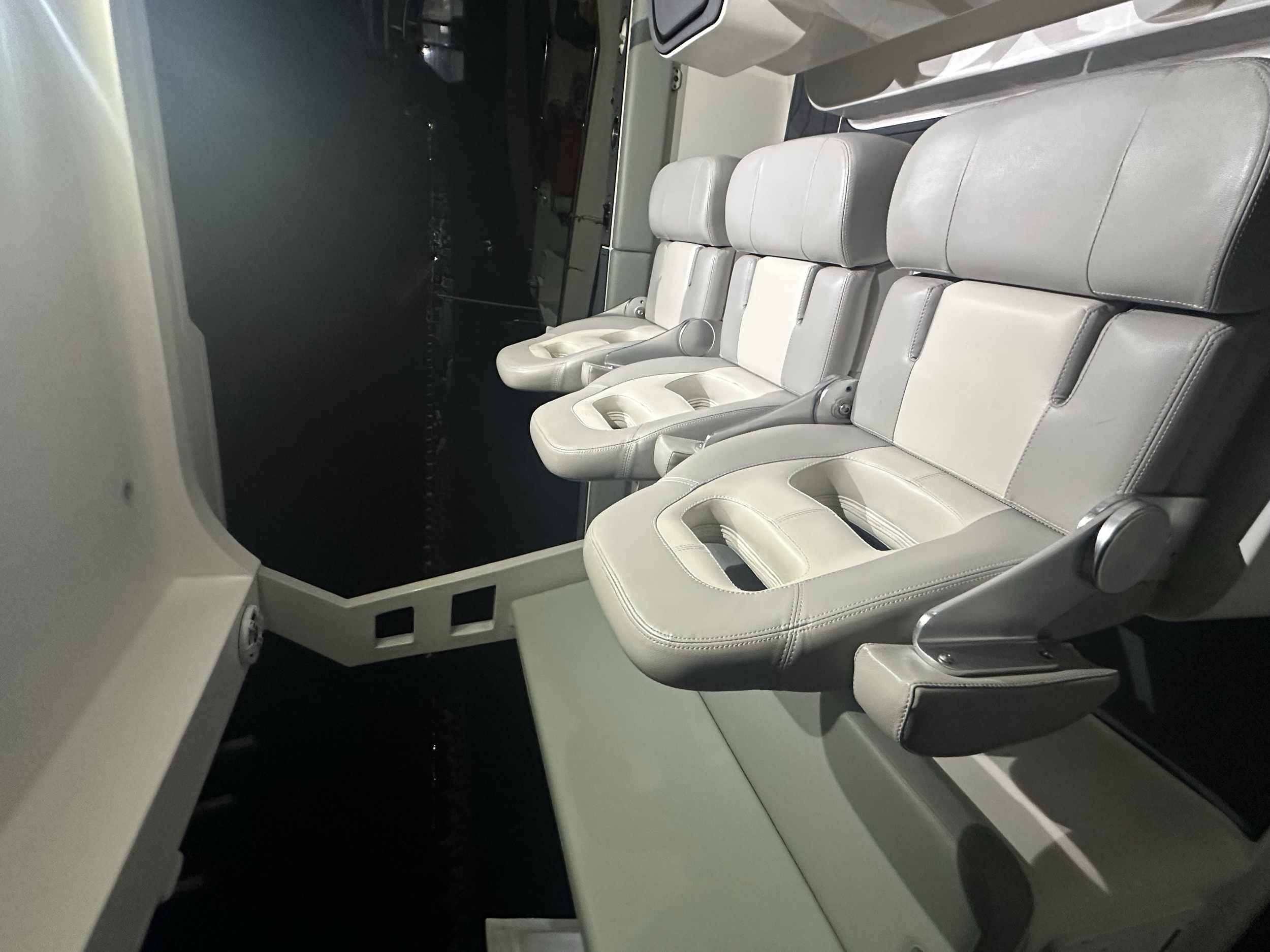 Interior view of the cockpit or control cabin of an aircraft with a row of beige leather seats and a large window showing night sky and city lights outside.