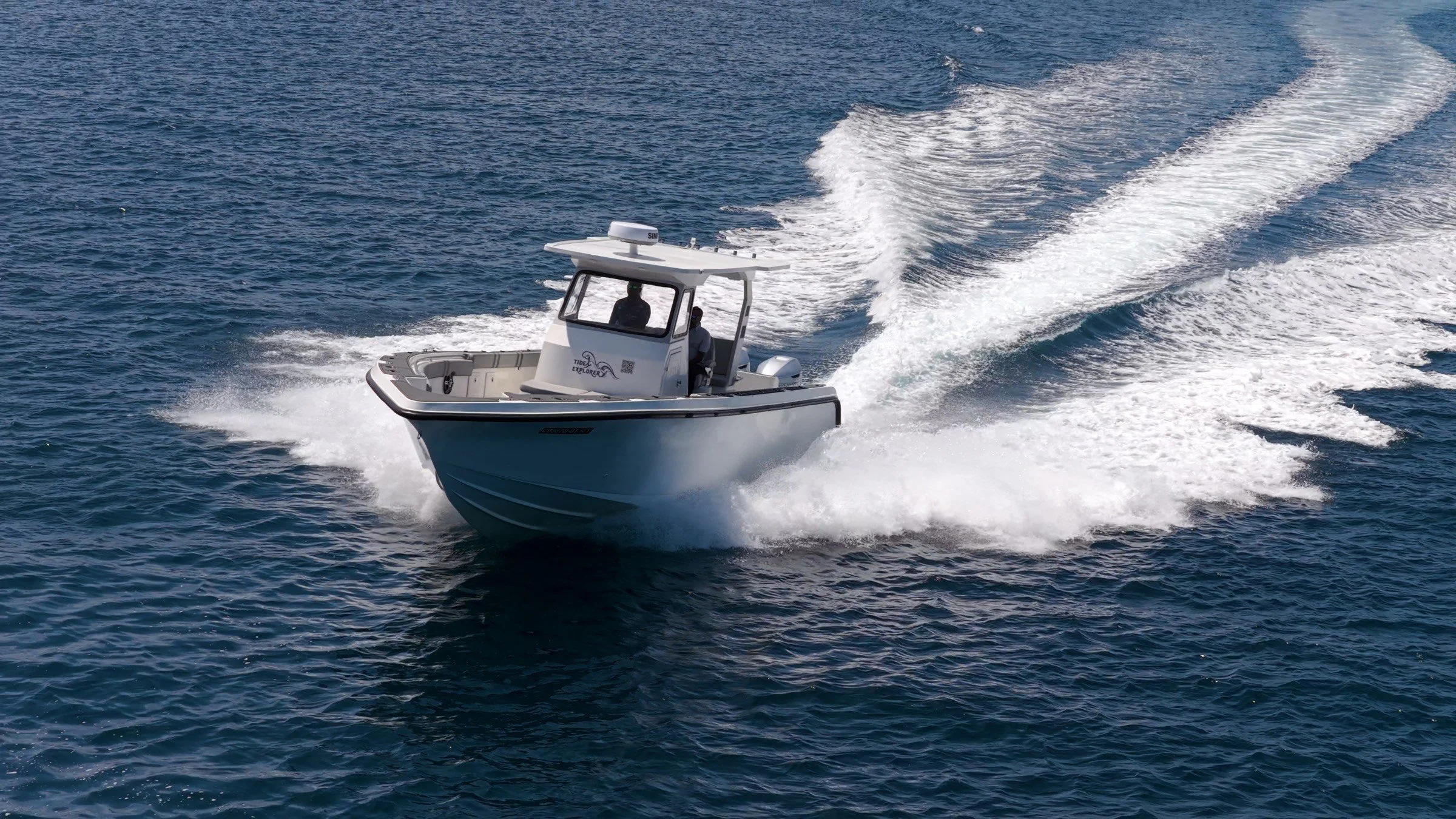 A small white motorboat speeding across the blue ocean, creating a trail of white frothy wake behind it.
