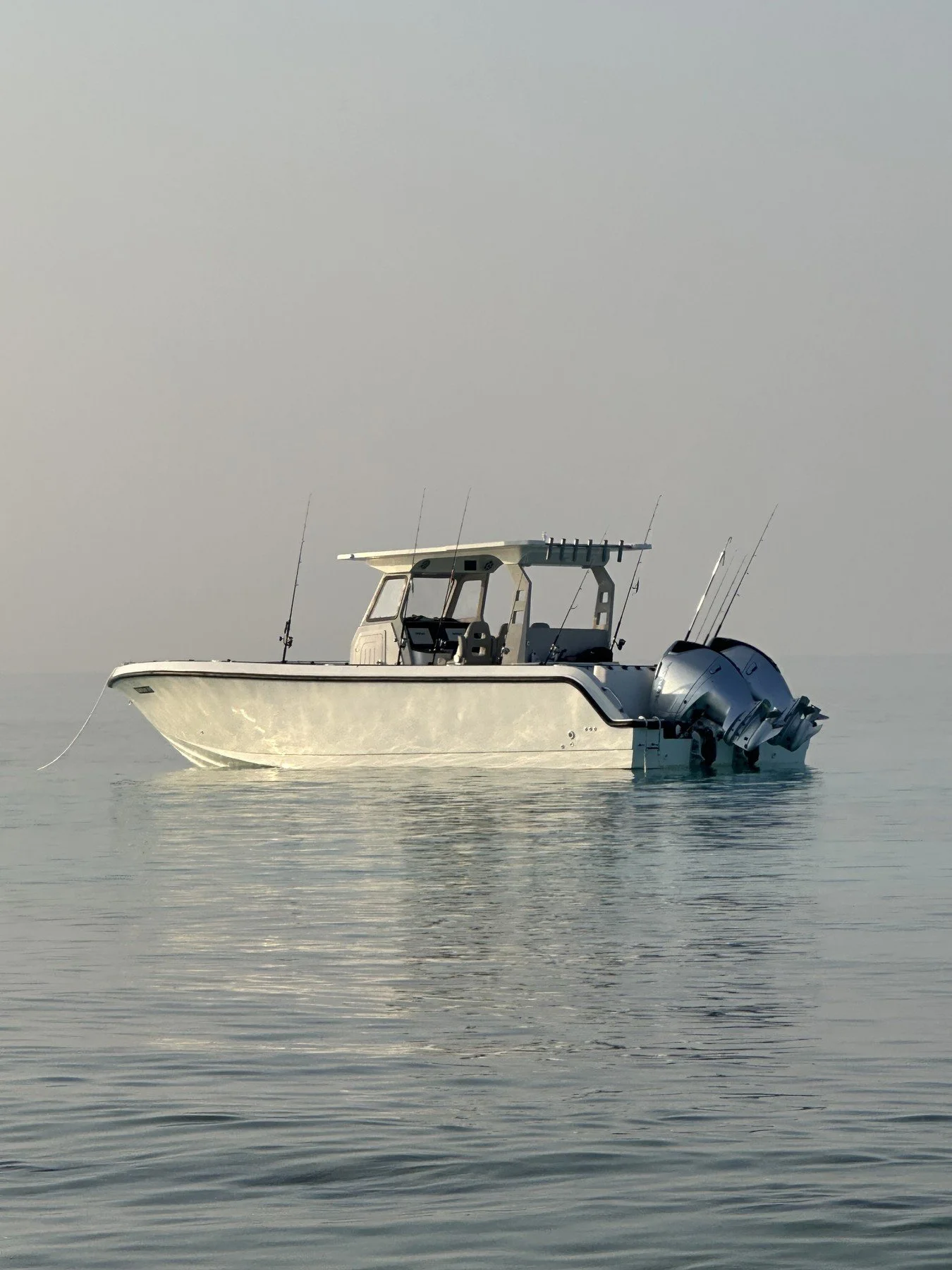 A white motorboat with dual engines floating on calm water, under a light gray sky.