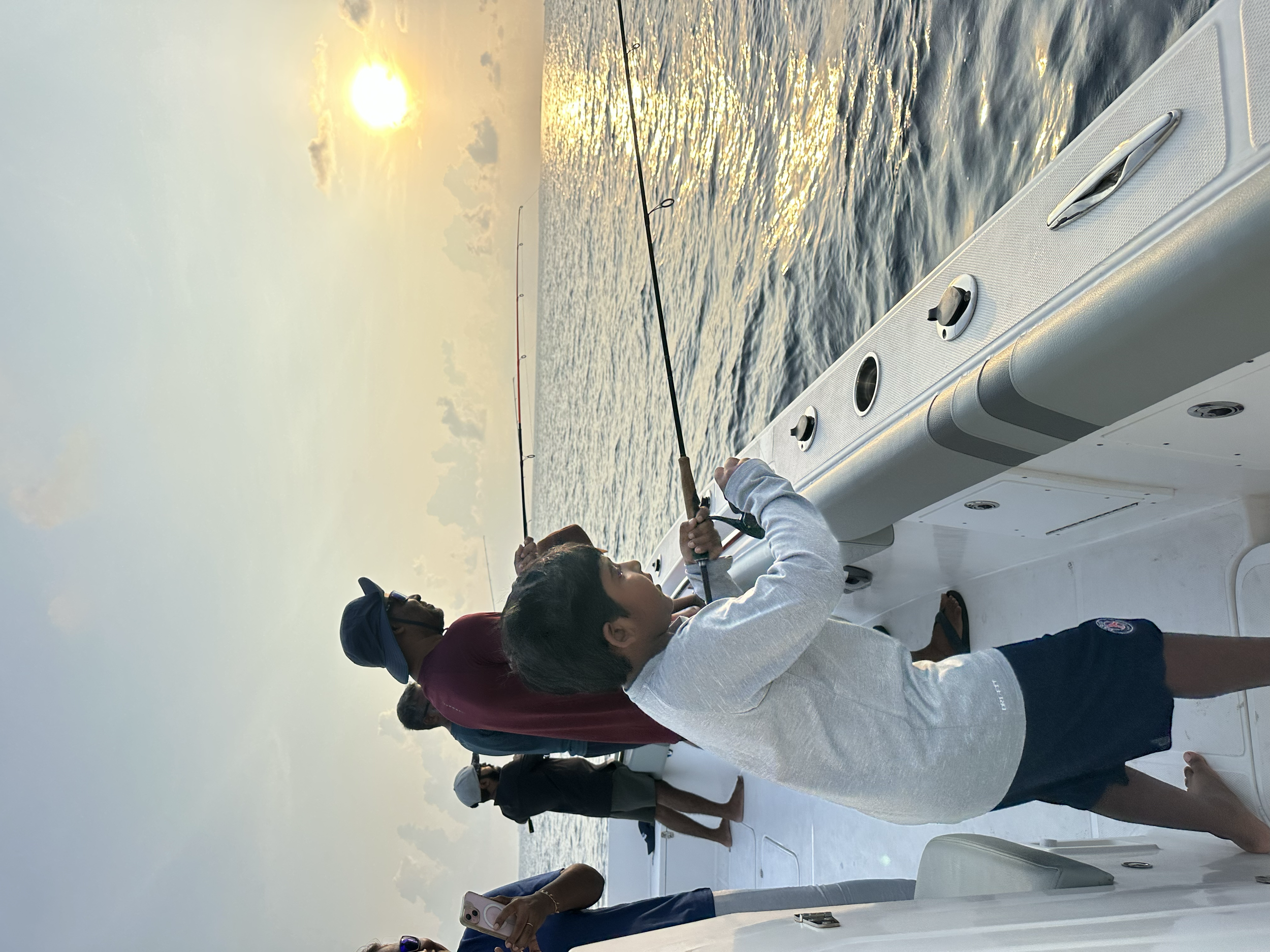 A woman fishing on a boat during sunset with other people aboard, on a calm body of water.