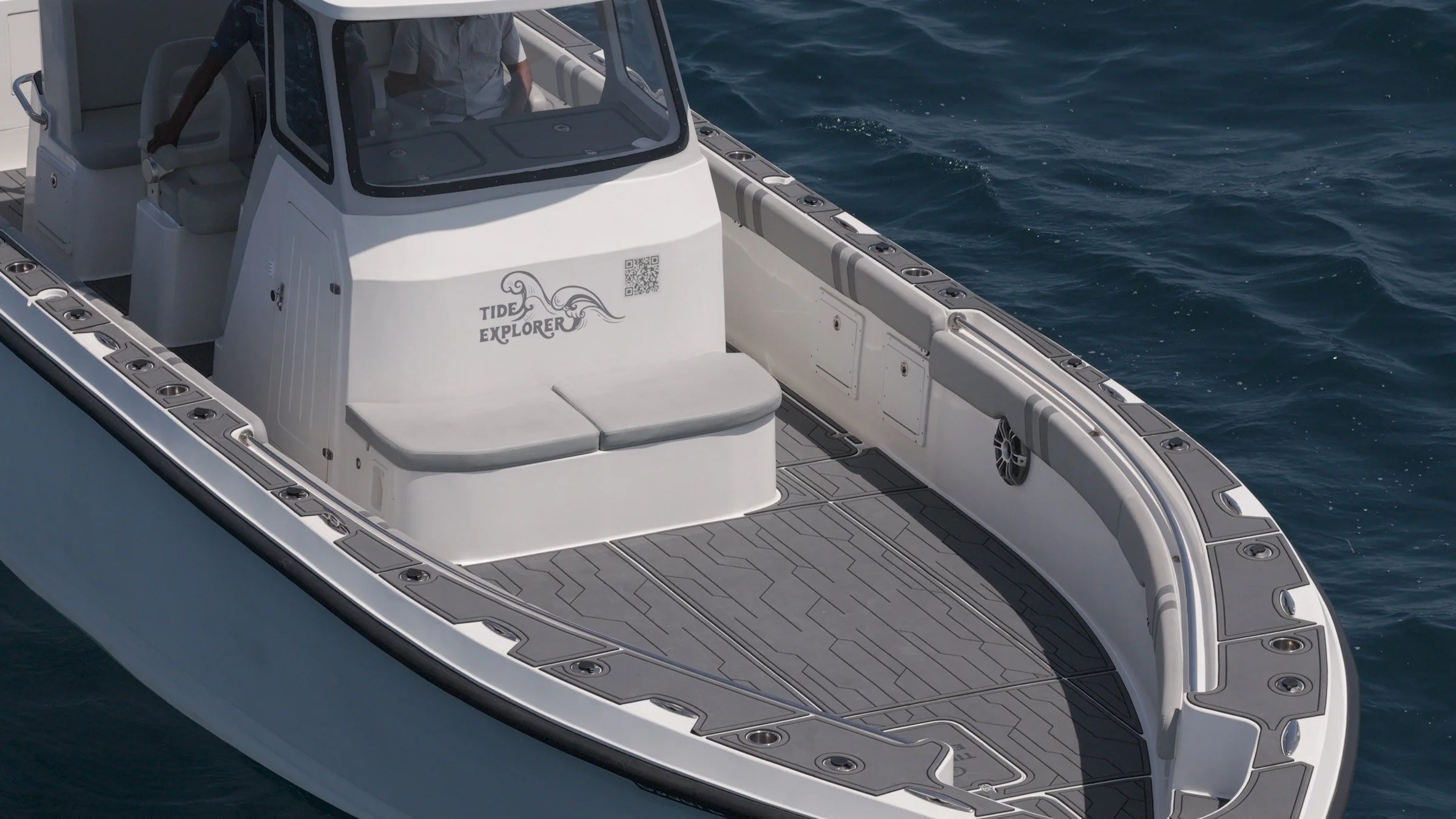 A white yacht on the water with a shaded cockpit area, a bench seat, speakers, and a logo that reads 'Tide Explorer' on the front.