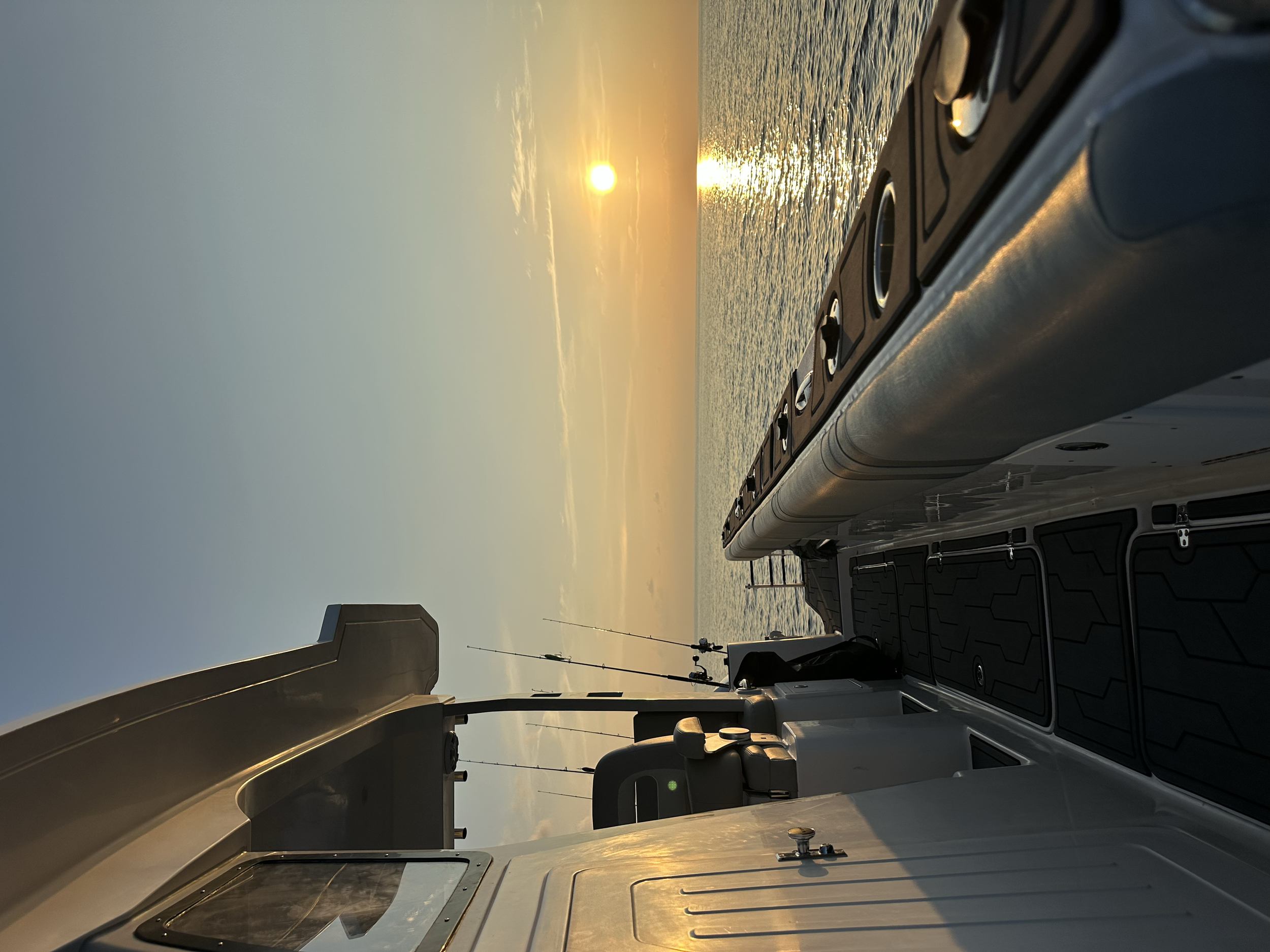 View of the ocean during sunset from a boat, showing the boat's dashboard, steering wheel, and antennas.