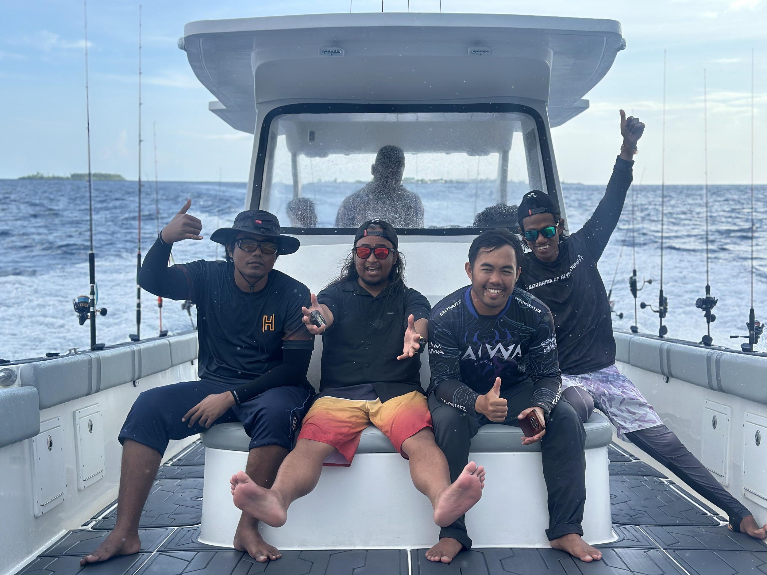 Four friends enjoying a boat ride on the ocean, smiling and posing for the camera, with fishing rods attached to the boat and a small island visible in the background.