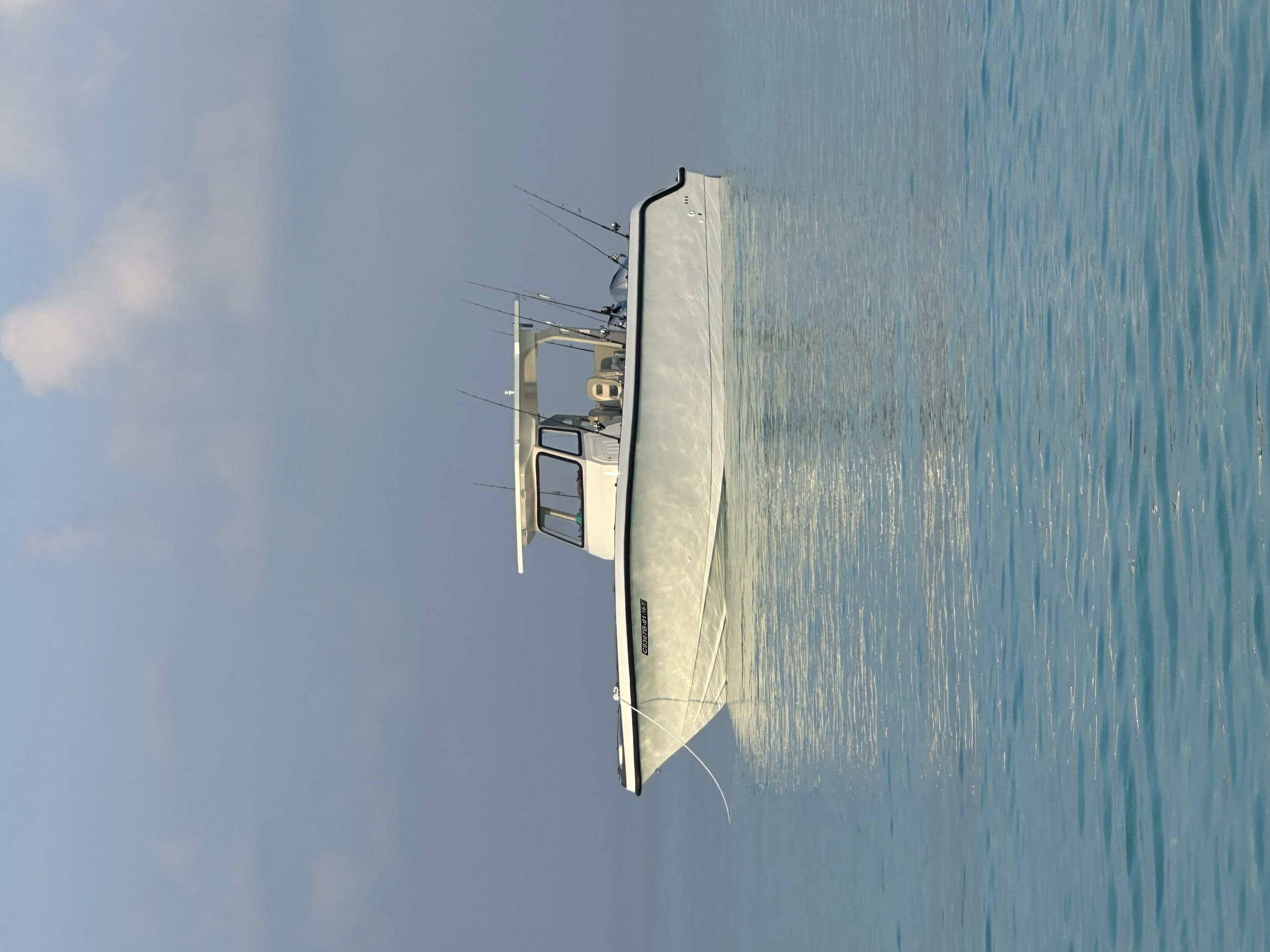 A white yacht floating on calm blue water with a slightly cloudy sky in the background.