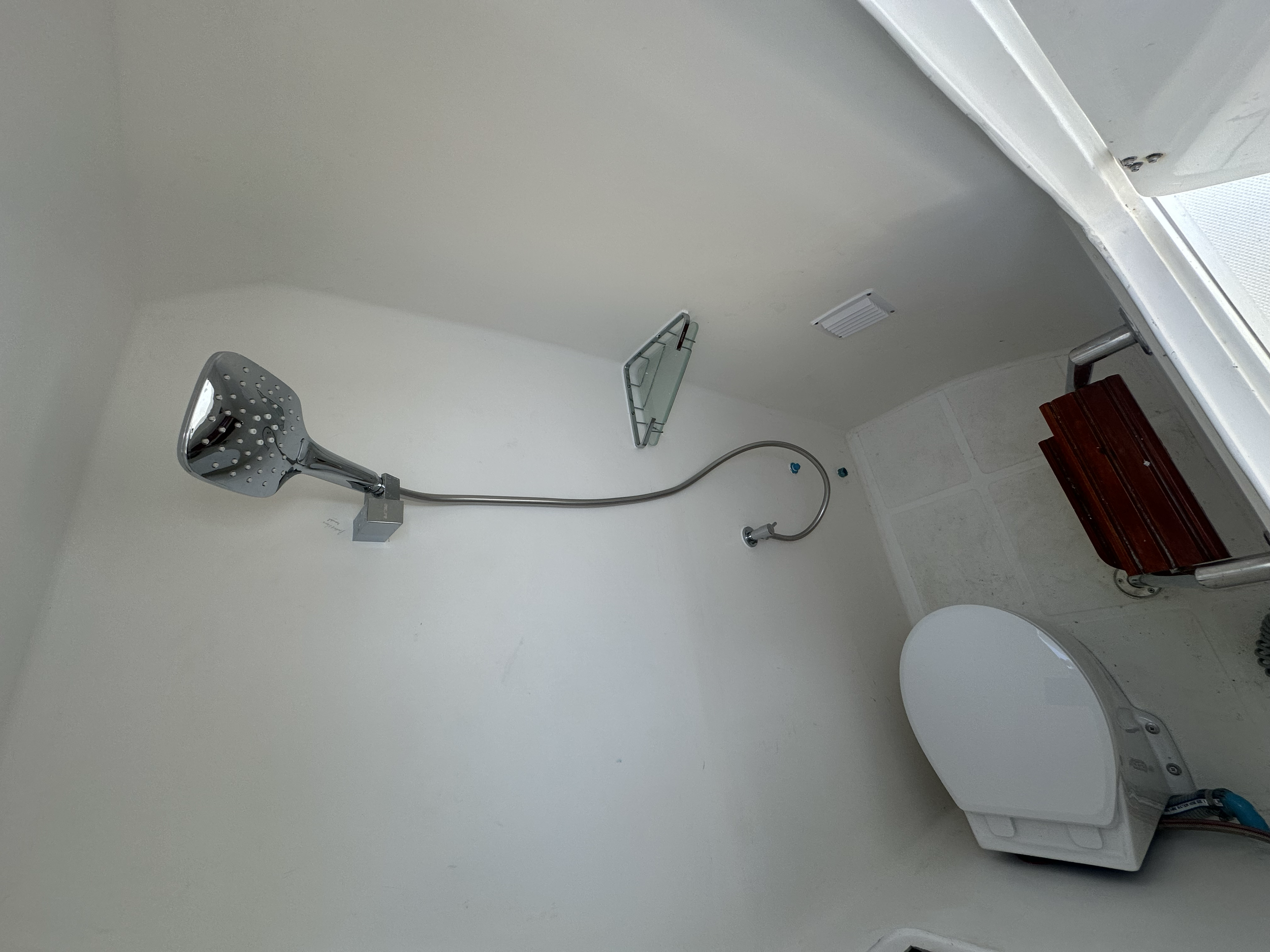 Empty bathroom with showerhead installed on the wall, a glass shelf, a small wooden stool, and a washing machine.