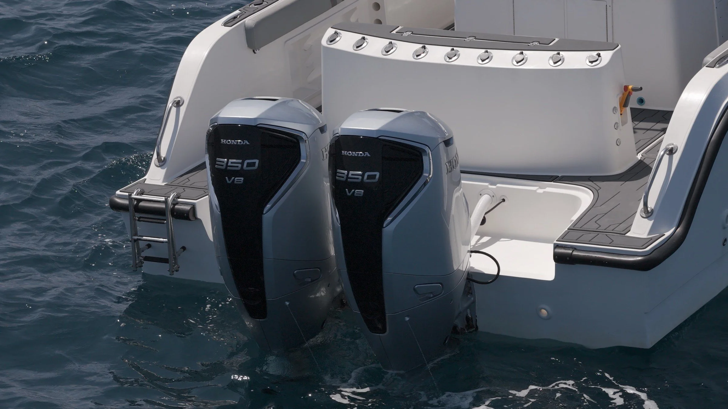 Close-up of the stern of a yacht with two Honda 350 V8 outboard motors, part of the deck, and the ocean water surrounding it.