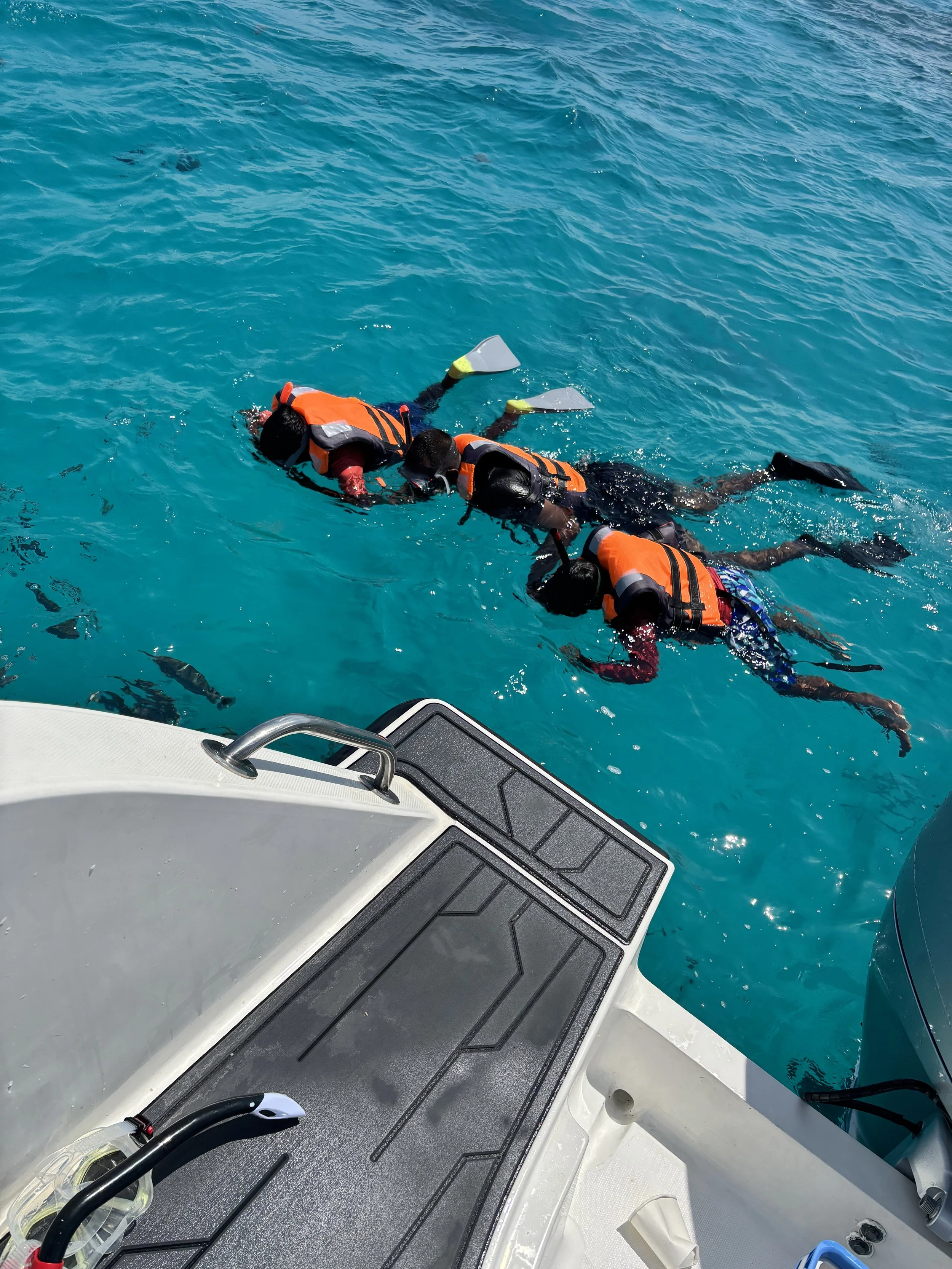 Two people wearing life jackets snorkeling in the ocean near a boat.