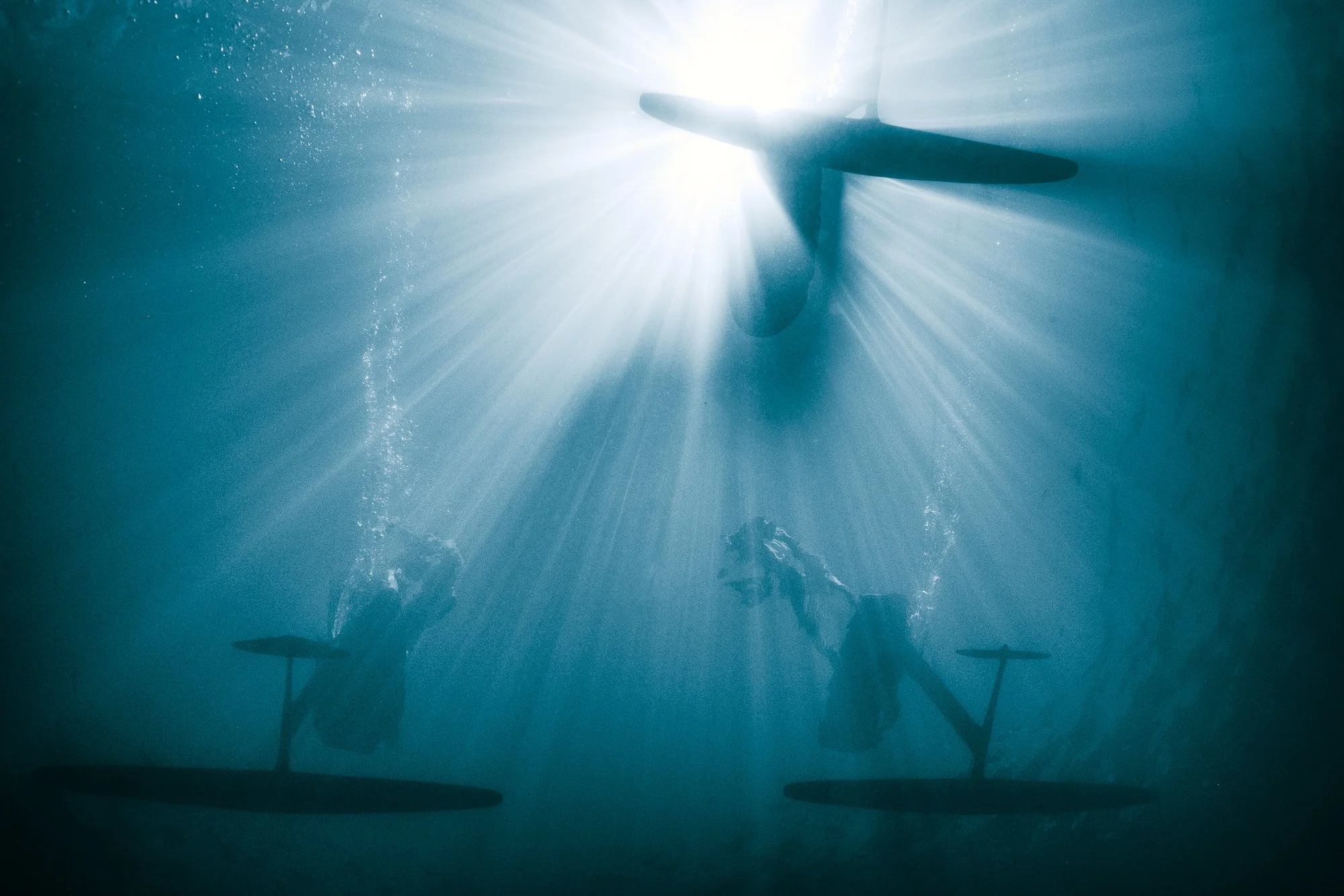 Trois foil sous l'eau avec des planches de Pumpfoil, la lumière du soleil filtrant à travers la surface de l'eau.
