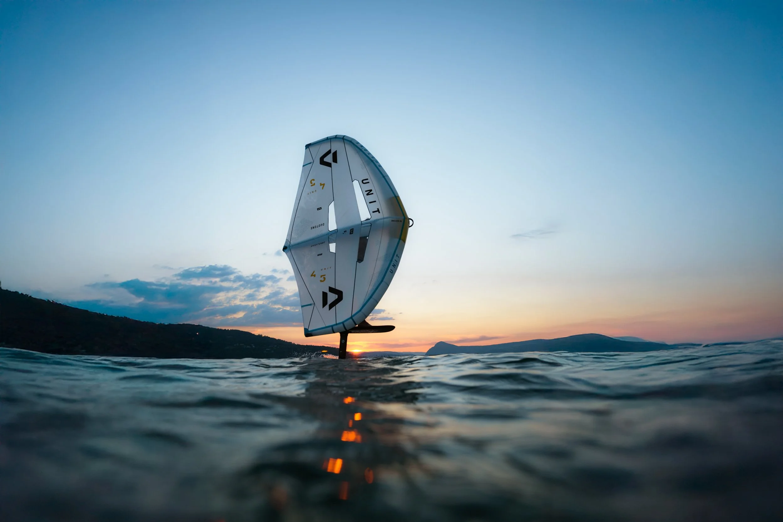 Planche de Wing foil flottant près de l'eau avec coucher de soleil en arrière-plan