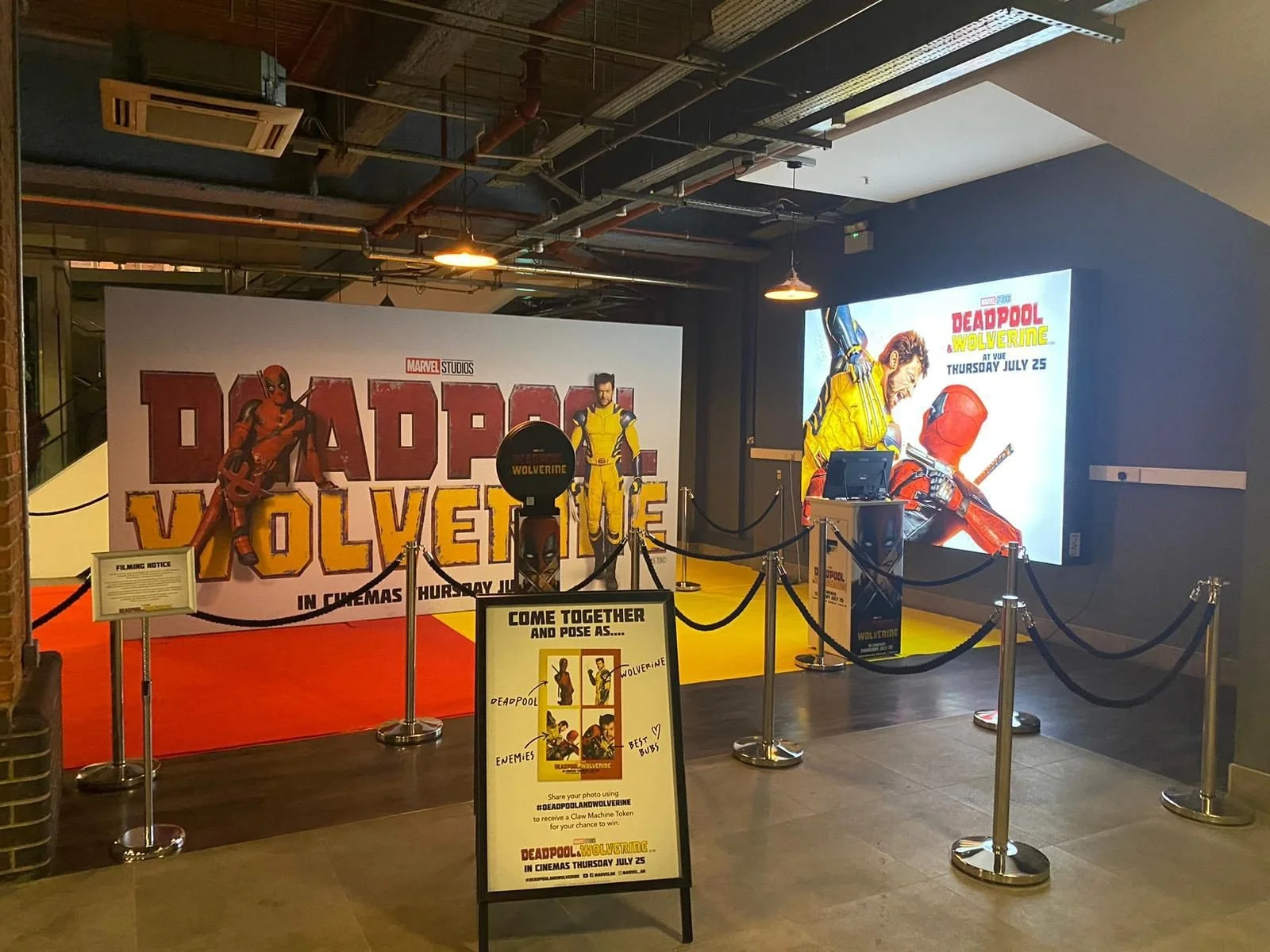 Display promoting the movie Deadpool & Wolverine, including a large backdrop with Deadpool and Wolverine characters, a large digital screen with artwork, and a sign encouraging photo taking with Deadpool and Wolverine poses at the cinema entrance.