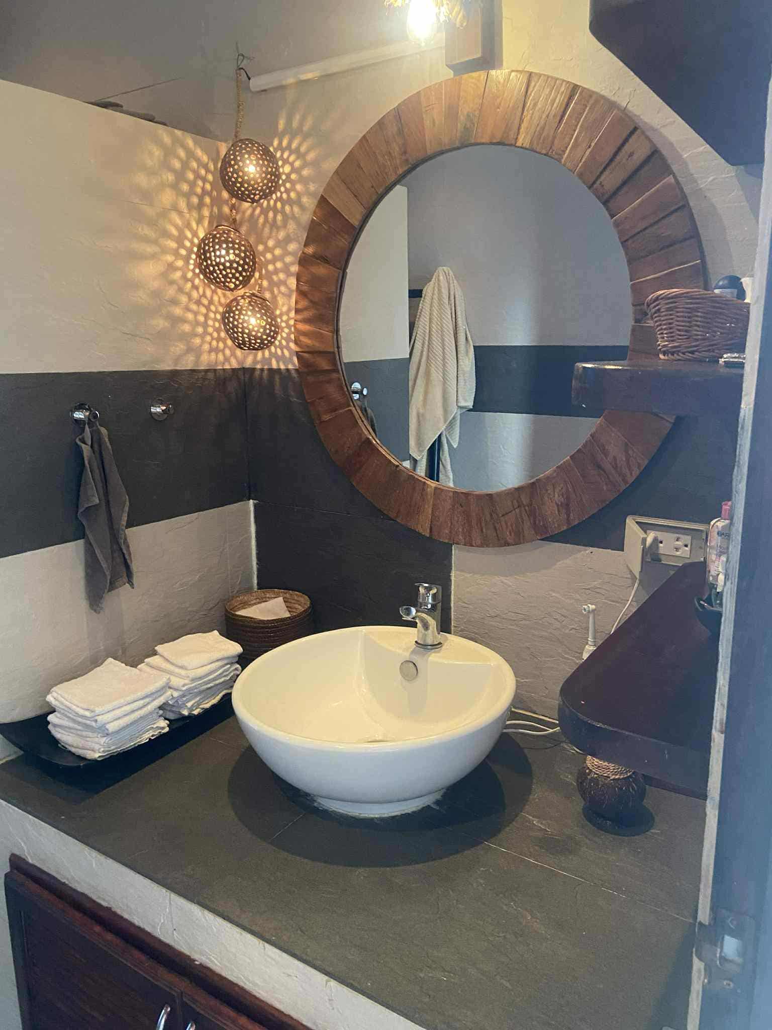 Bathroom with a round mirror, a white vessel sink, folded towels, and a decorative hanging light fixture.
