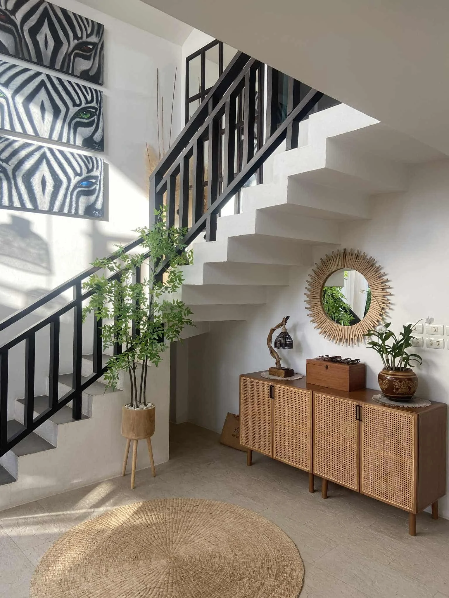 Interior view of a modern home with staircase, wooden cabinet, mirror, potted plant, and artwork with zebra patterns.