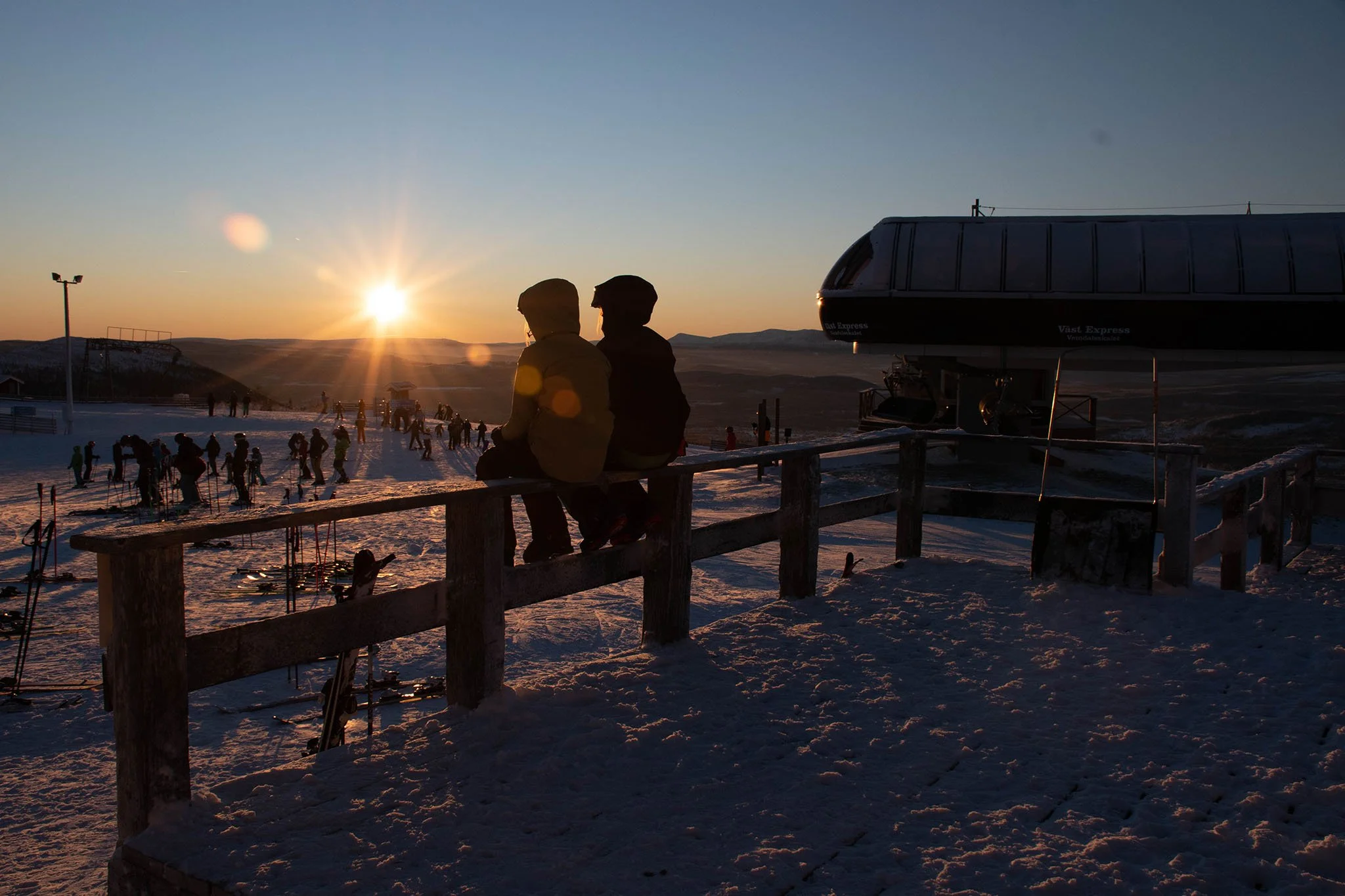 Två barn som sitter på ett staket uppe på fjället i solnedgången - företagsfoto av byMalott