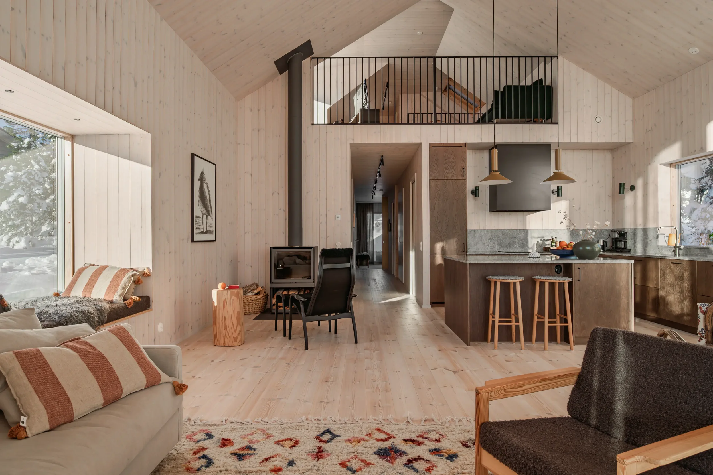Ljust vardagsrum och kök med träpanel, braskamin och loft i ett fjällhus i Storhogna, fotograferat av Malin Lennartzon.
