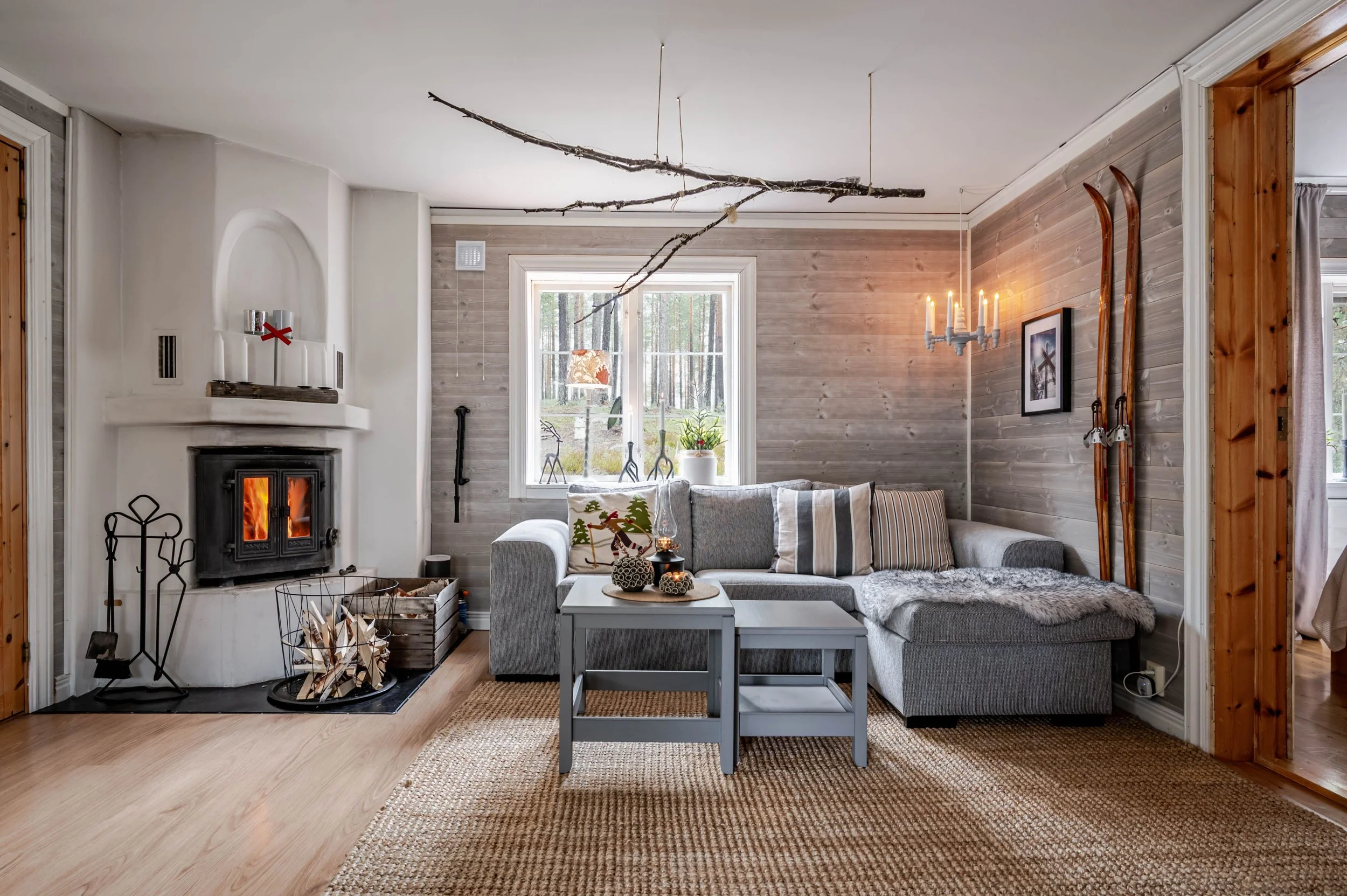 Ljust vardagsrum i fjällboende med braskamin, soffa och trädetaljer, fotograferat av byMalott