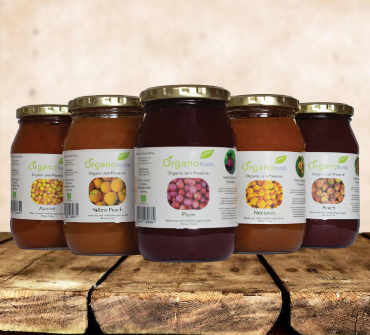 Five jars of organic jam preserves with labels for apricot, yellow peach, plum, nectacot, and peach, displayed on a wooden surface.