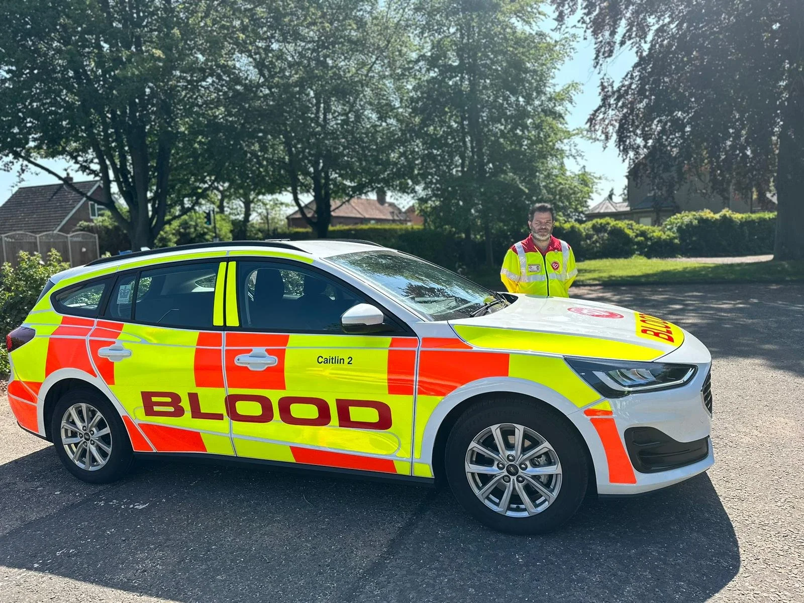 A male volunteer with a beard wearing a red and yellow high-visibility safety jacket