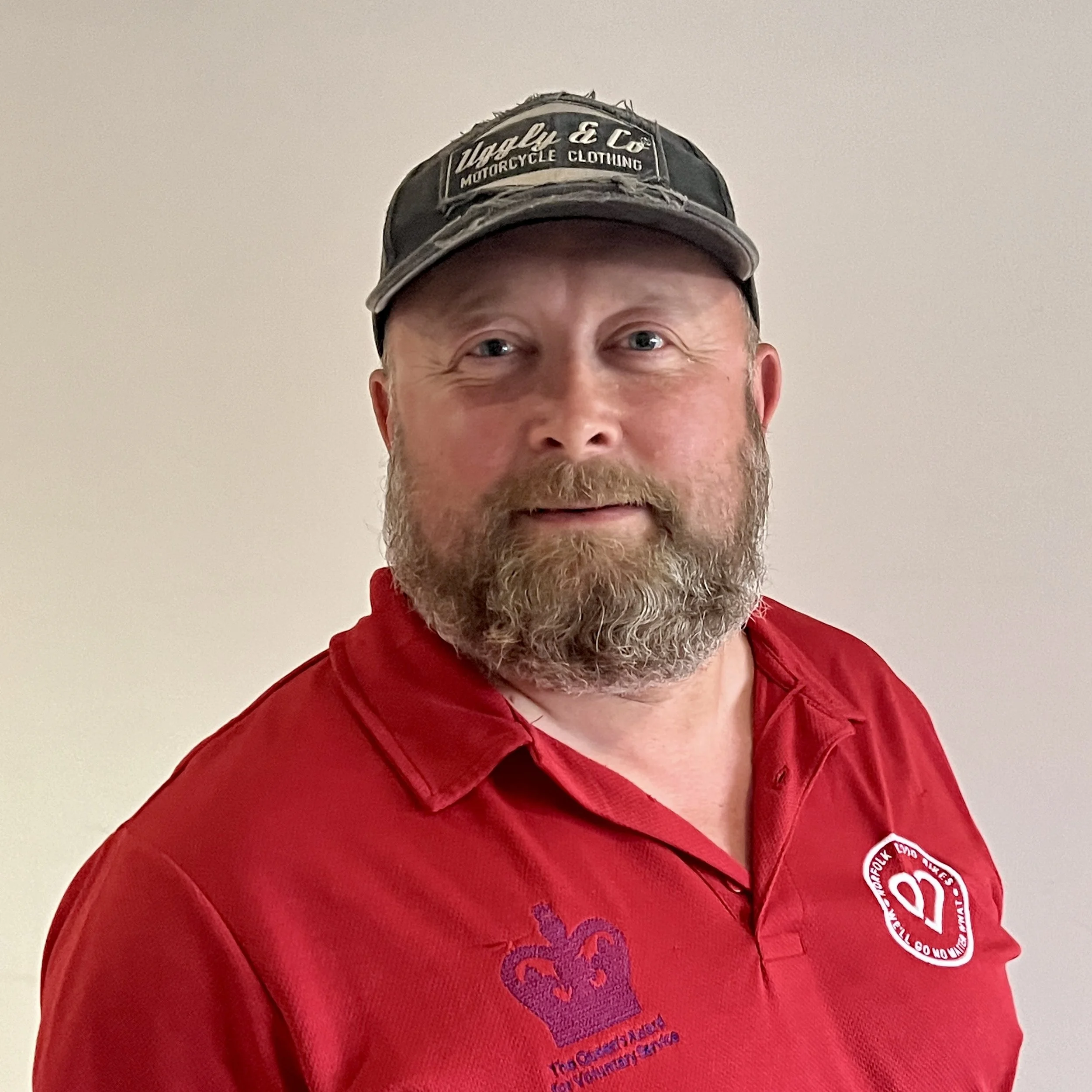 A male volunteer in a yellow high-visibility jacket standing next to a police motorcycle with a windshield that has a red "BLOOD" sticker. He is smiling and is outdoors on a residential street with houses and trees in the background.