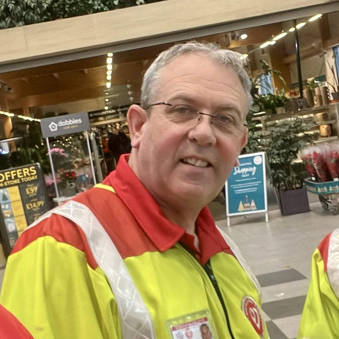 A volunteer wearing a high-visibility yellow and red jacket standing outside a building.