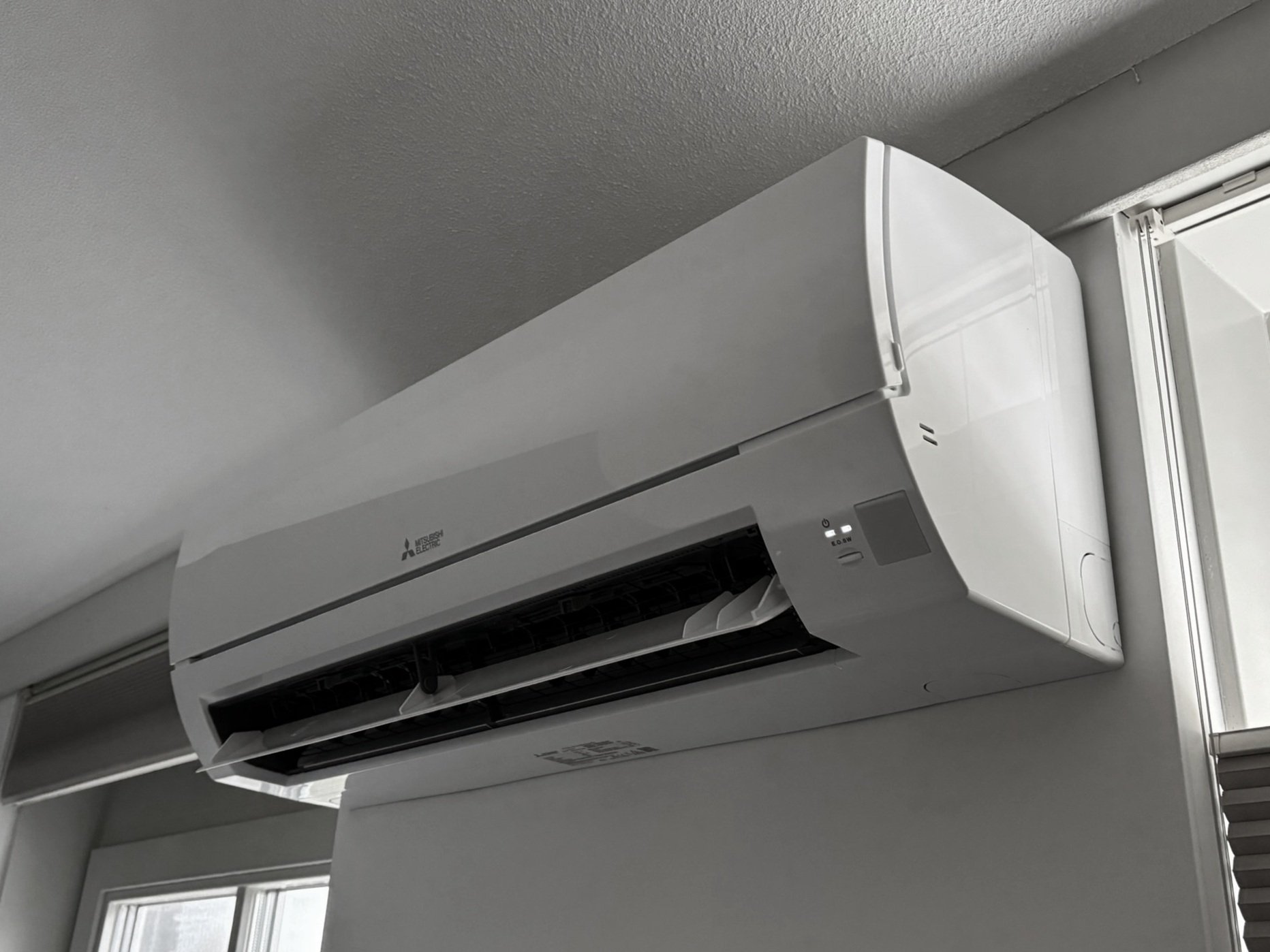 Een witte Mitsubishi Electrics airconditioner bevestigd aan de muur, boven een raam.
