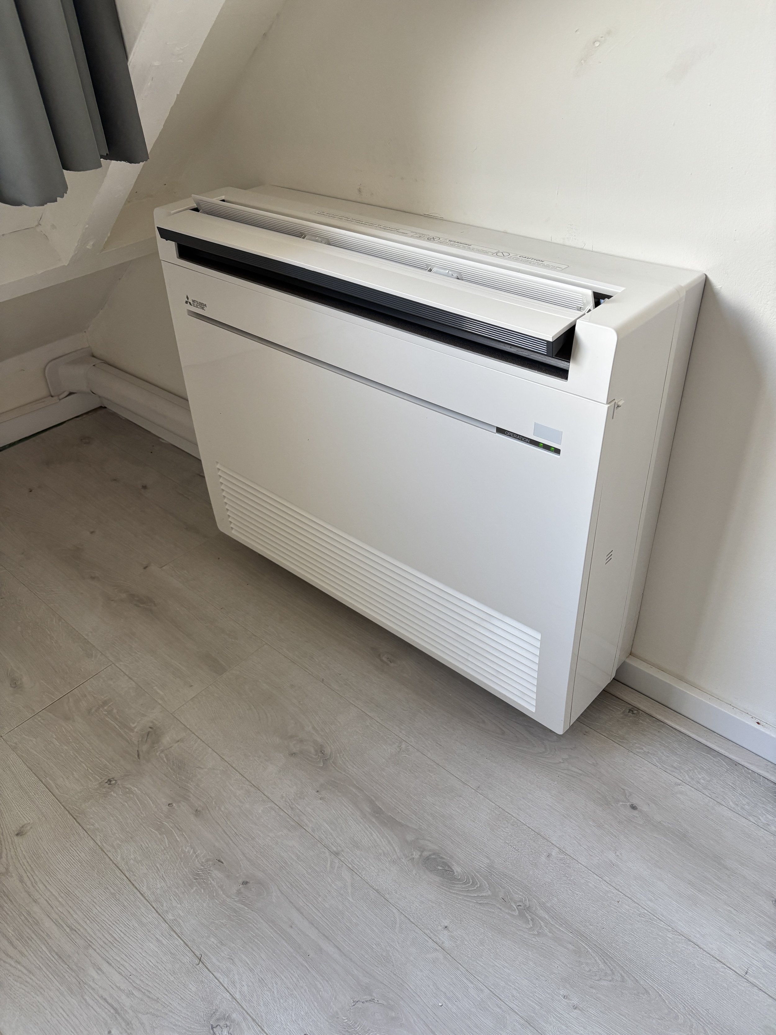 Elektrische convector verwarming op een houten vloer in een kamer met witte muren.