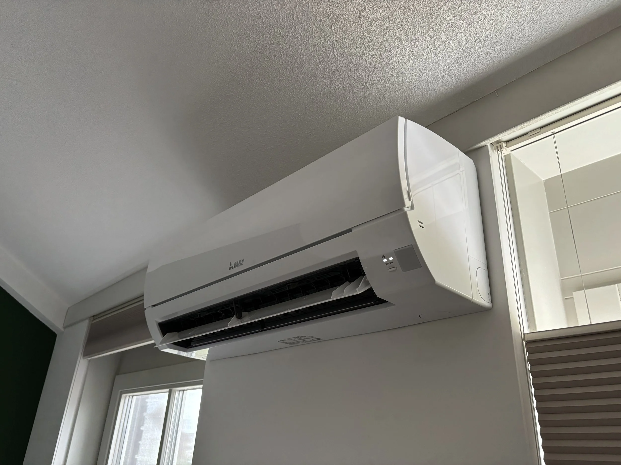 Remeha Mitsubishi airconditioner unit geïnstalleerd aan het plafond naast een raam met verticale blinds.