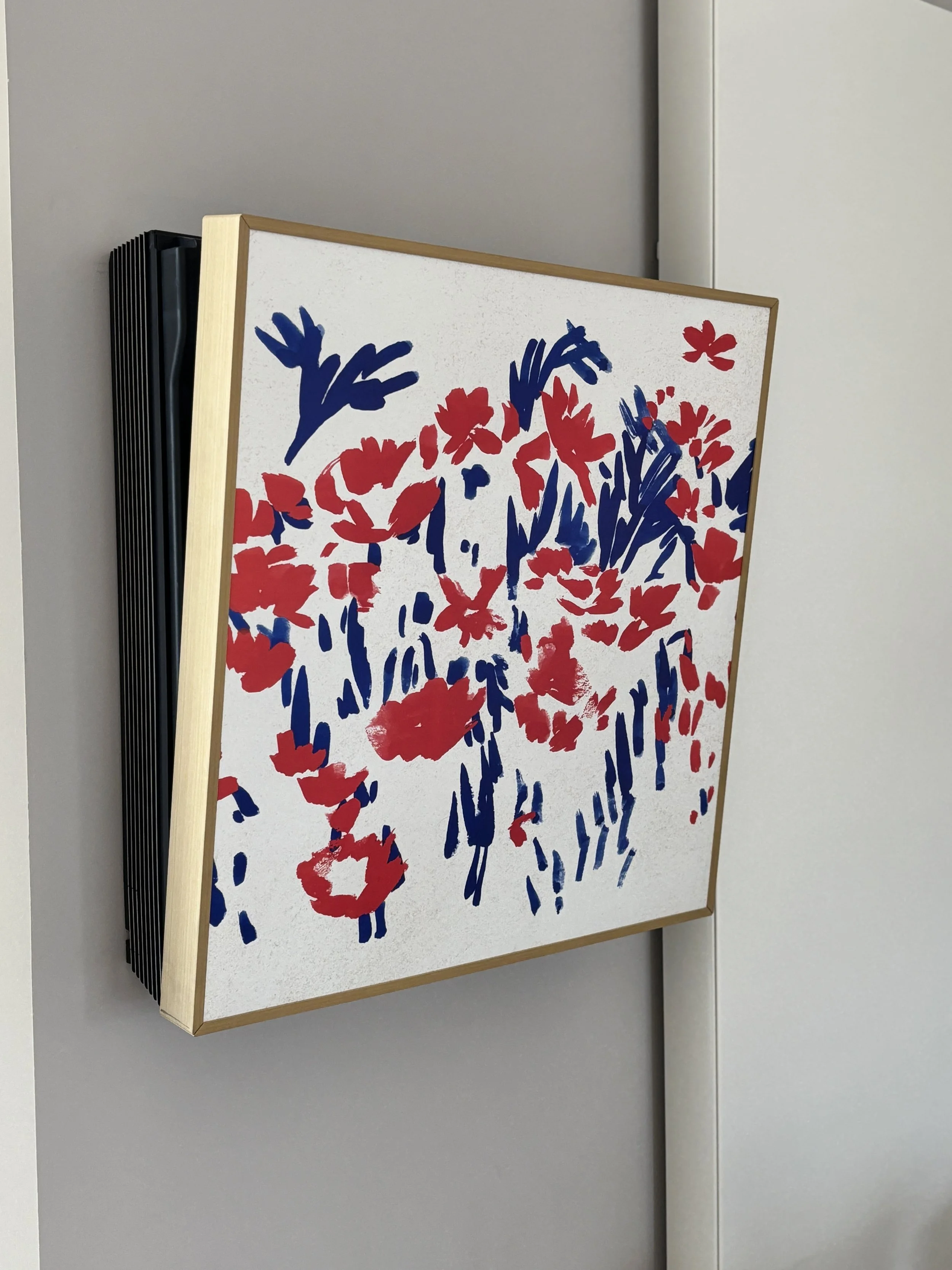 Kunstwerk met rode en blauwe bloemen op wit doek, gemonteerd op kader, hangend aan muur.
