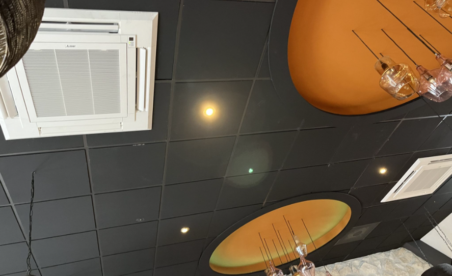 Ceiling with black tiles, round orange light fixtures, and hanging glass light bulbs.