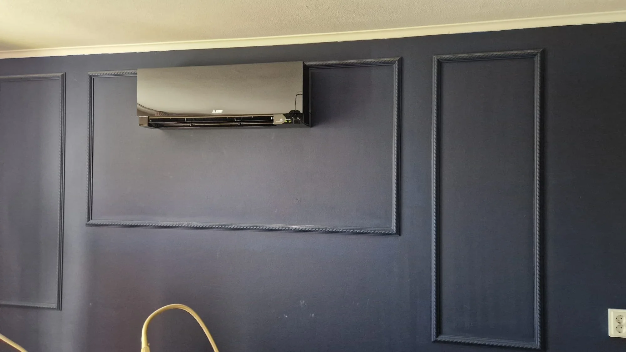 Donkere muur met decoratieve paneellijnen en een airconditioning unit aan de muur.