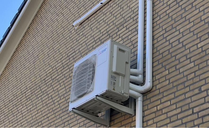 Een buitenunit van een airconditioningsysteem bevestigd aan een bakstenen muur.