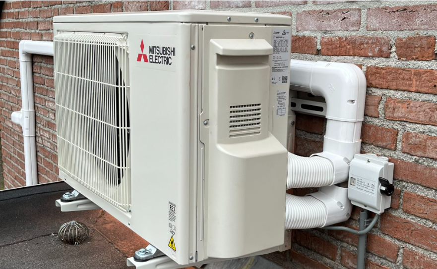 Een Mitsubishi Electric warmtepompinstallatie buiten gemonteerd aan een bakstenen muur.